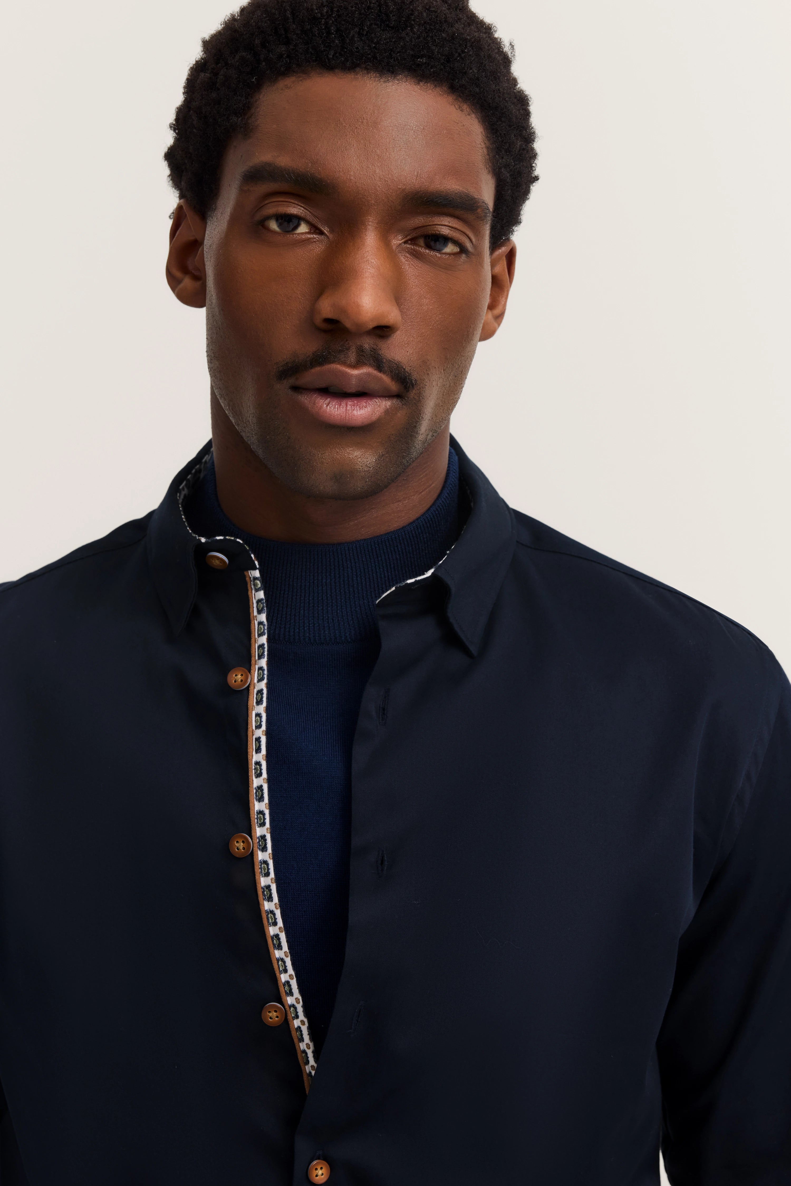 bugatti lifestyle: Man in dark blue shirt with contrast buttons, casual pose, embodies Italian elegance and sophistication.