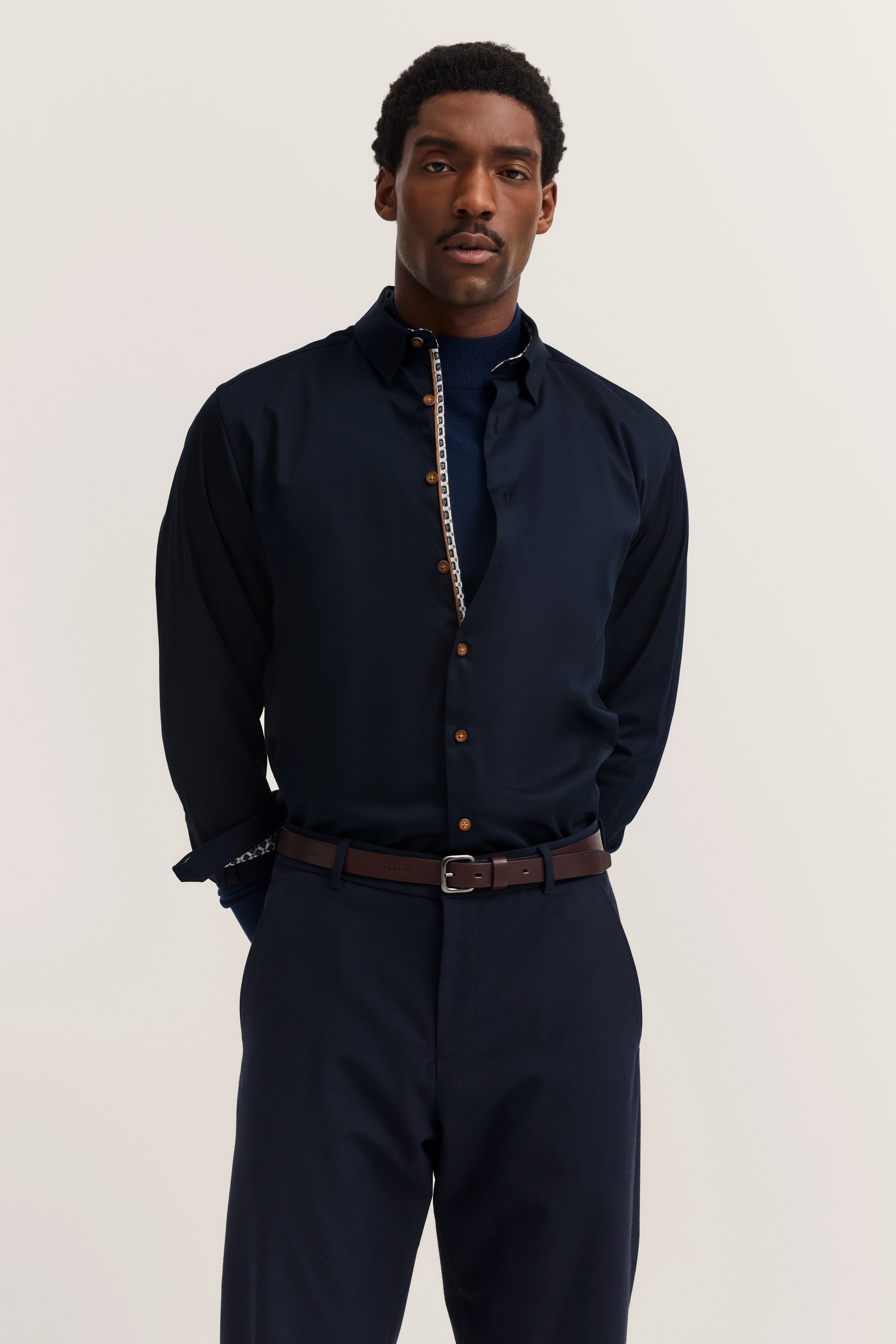 bugatti model: Dark blue shirt, brown belt, relaxed pose, timeless elegance.
