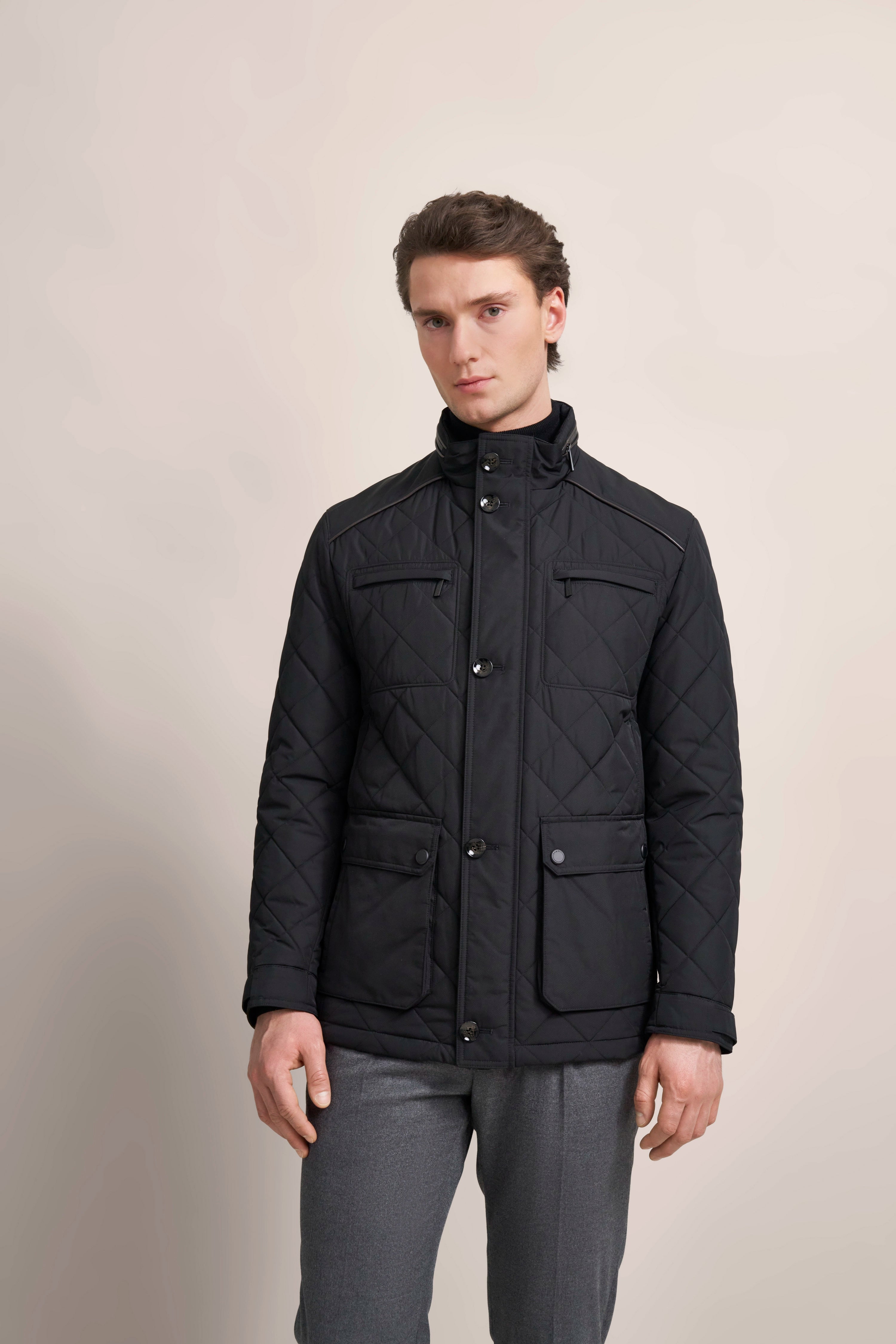 bugatti Modelbild: Schwarze Steppjacke, graue Hose, entspannte Pose, zeitloser Stil.