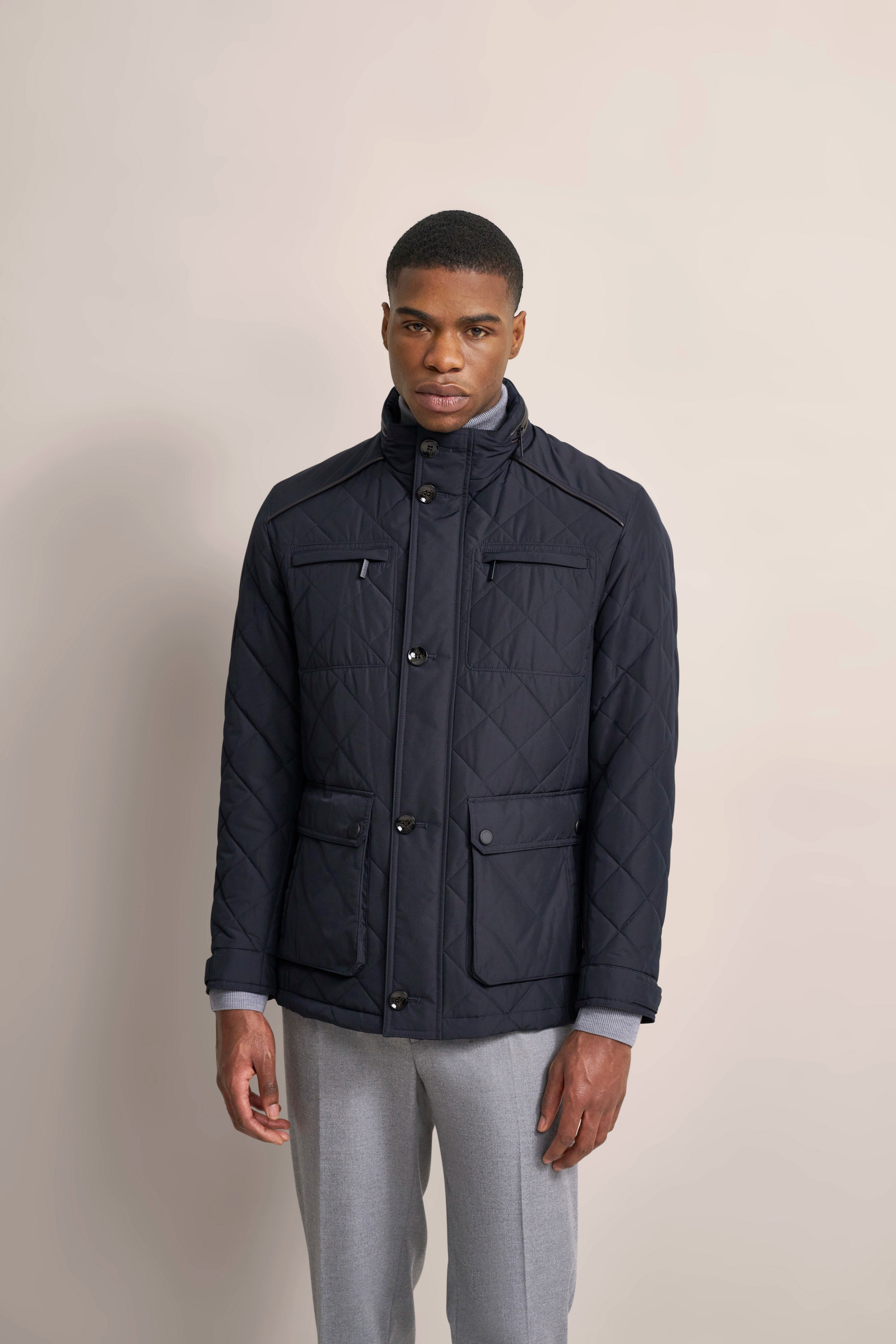 Modelbild mit schwarzer, gesteppten bugatti Jacke und grauer Hose, entspanntes Posing.