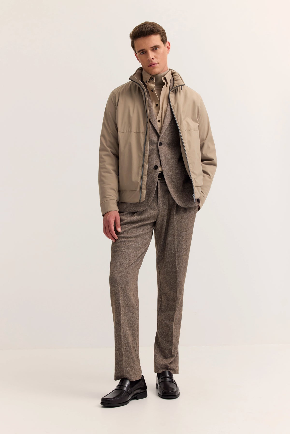 Model in beigefarbener Jacke, braunem Anzug und Hemd. Elegante Pose, entspannte Haltung.