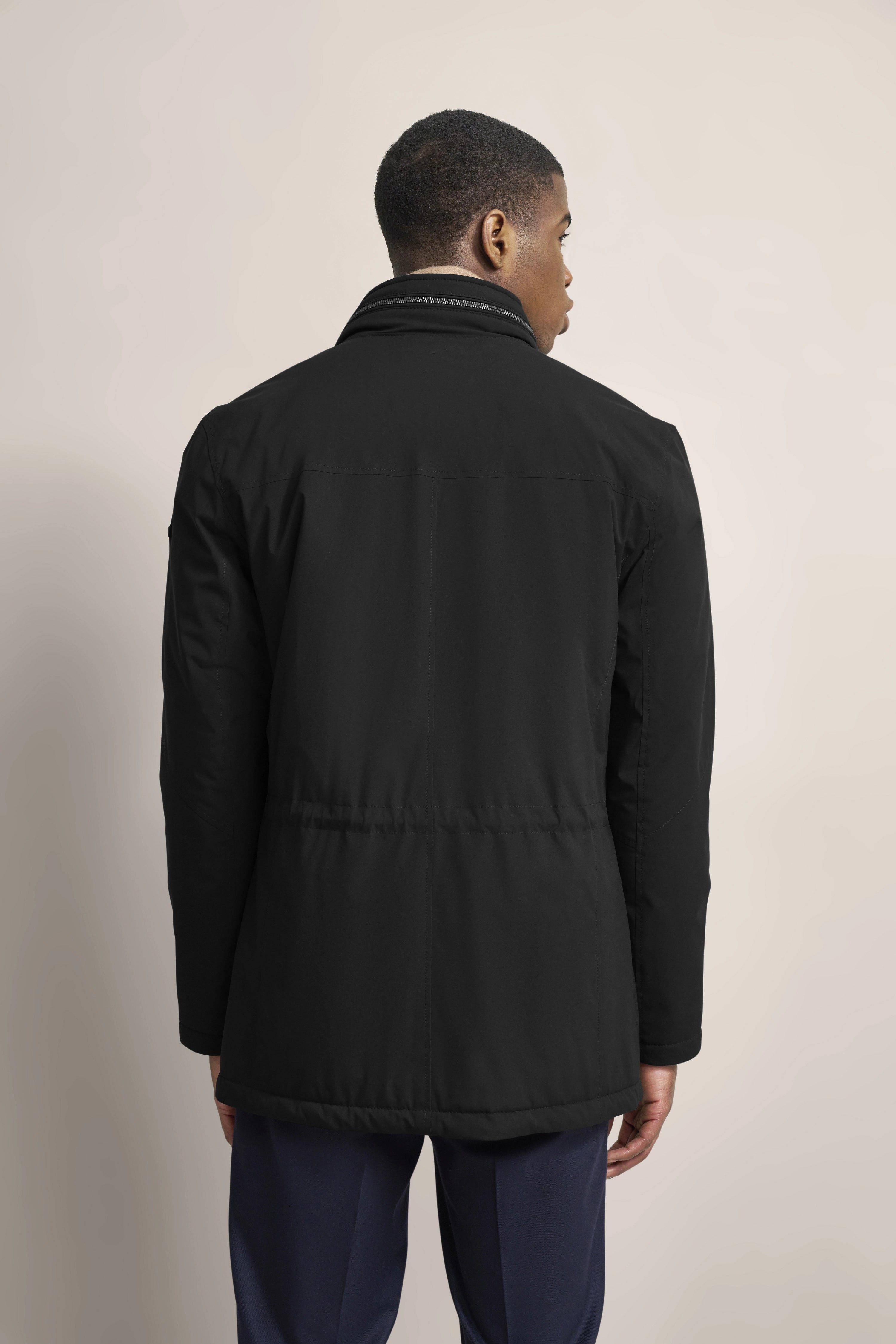 Schwarze bugatti Jacke, Rückansicht, über blauen Hosen. Modelbild, lässige Haltung.