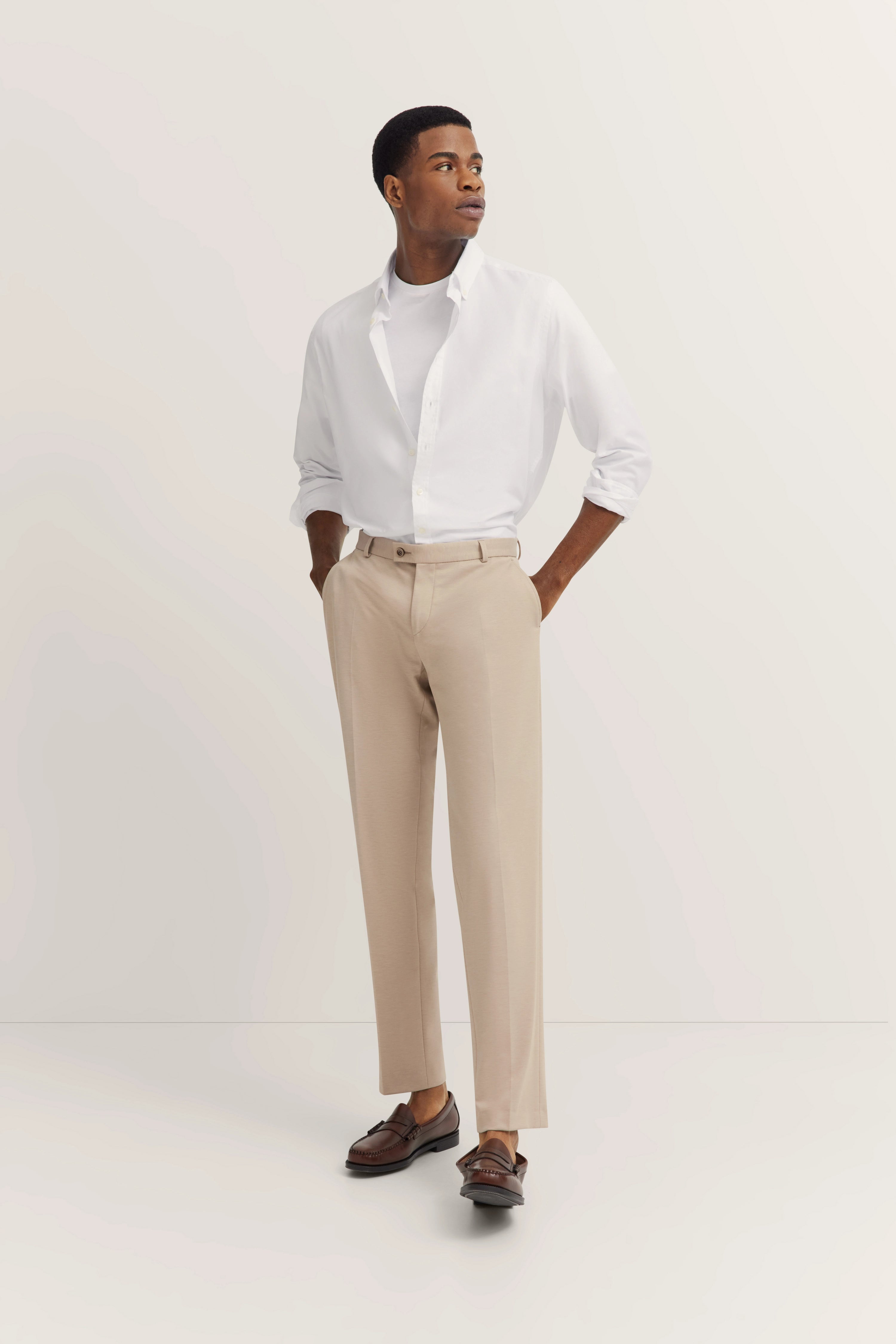 Model in weißem Hemd, beiger Hose, braunen Loafers, lässige Pose. Eleganter bugatti Look.