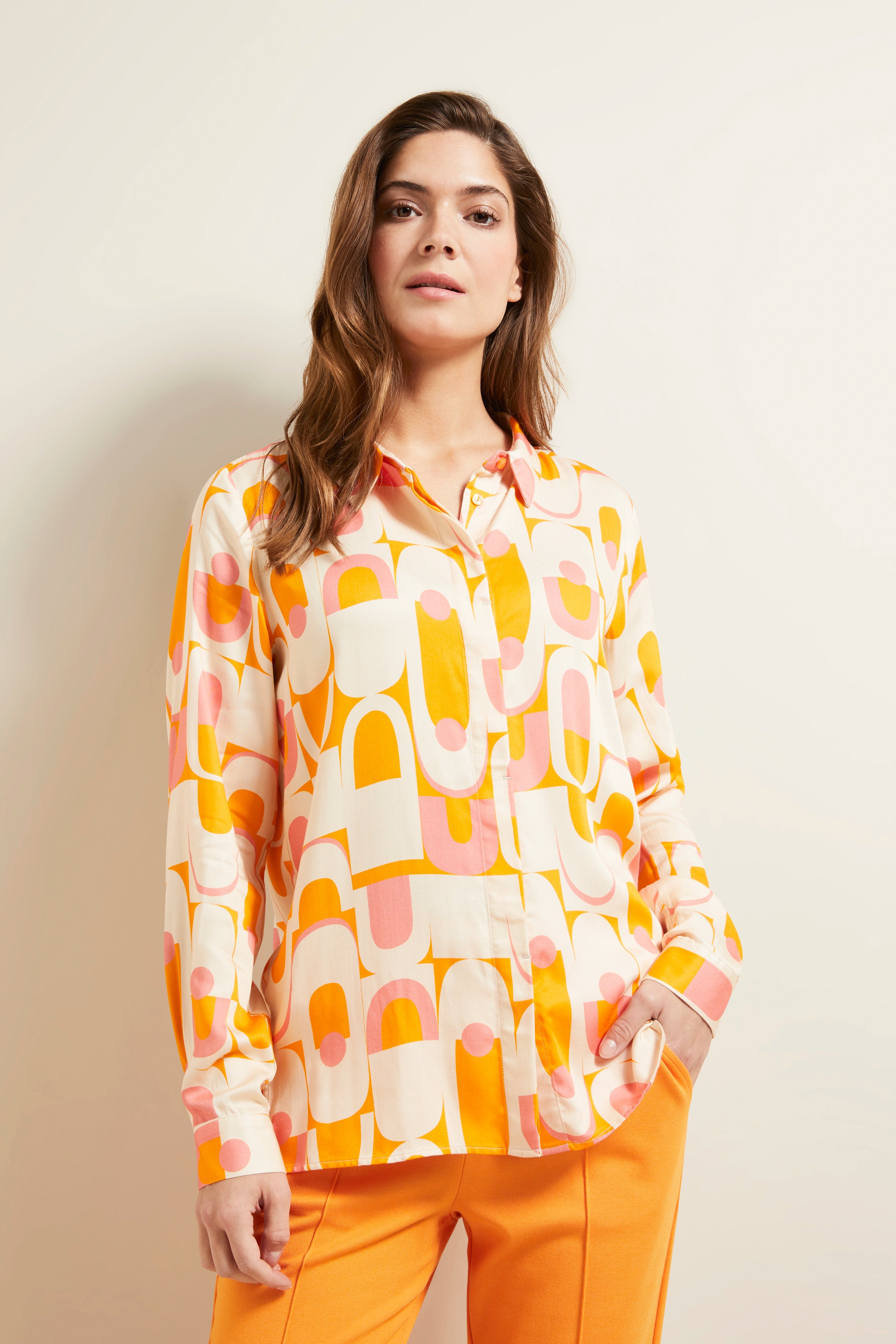 Colorful patterned blouse in orange and pink, model posing relaxed.