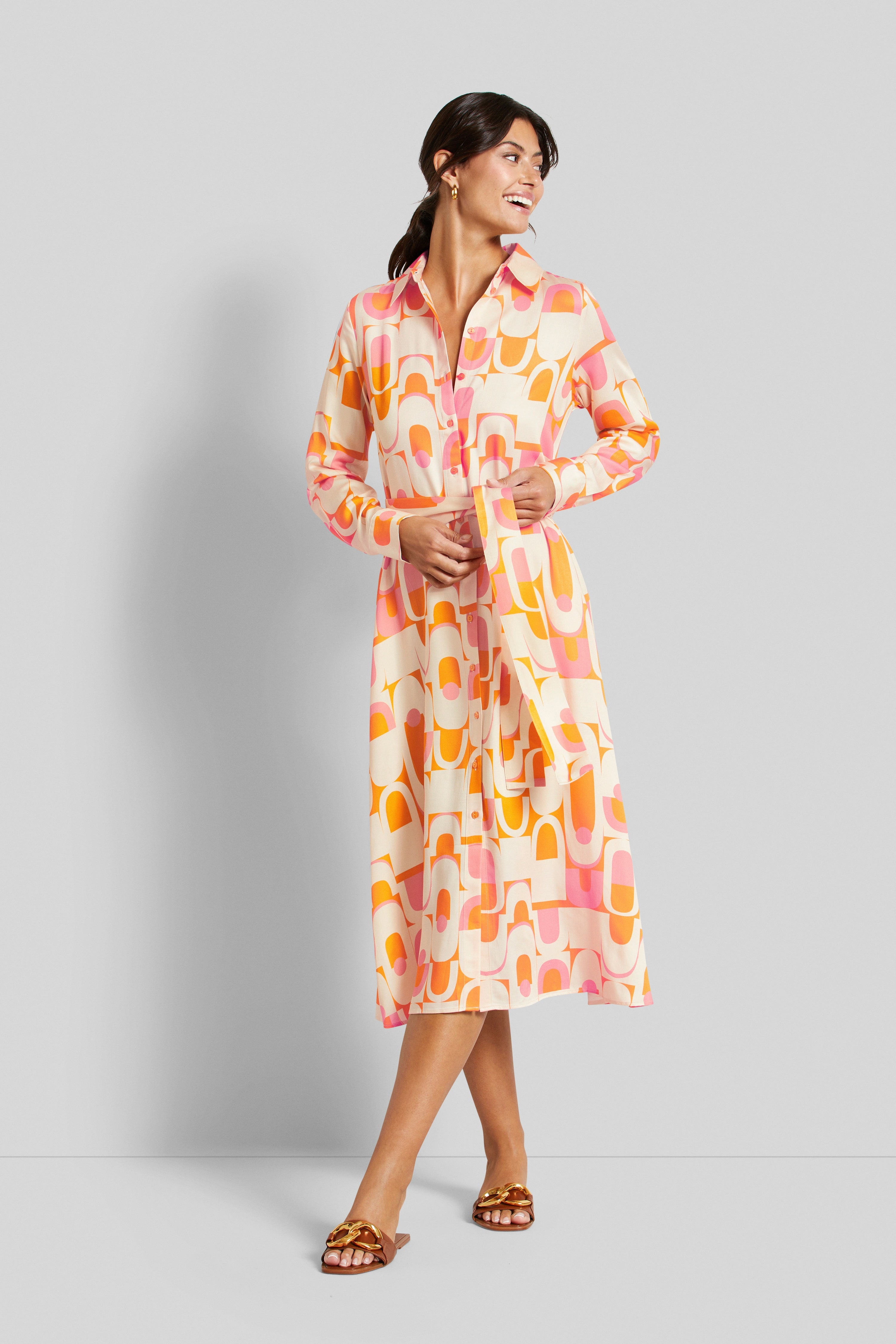 Model in colorful patterned bugatti shirt dress, smiling, standing sideways with tied belt.