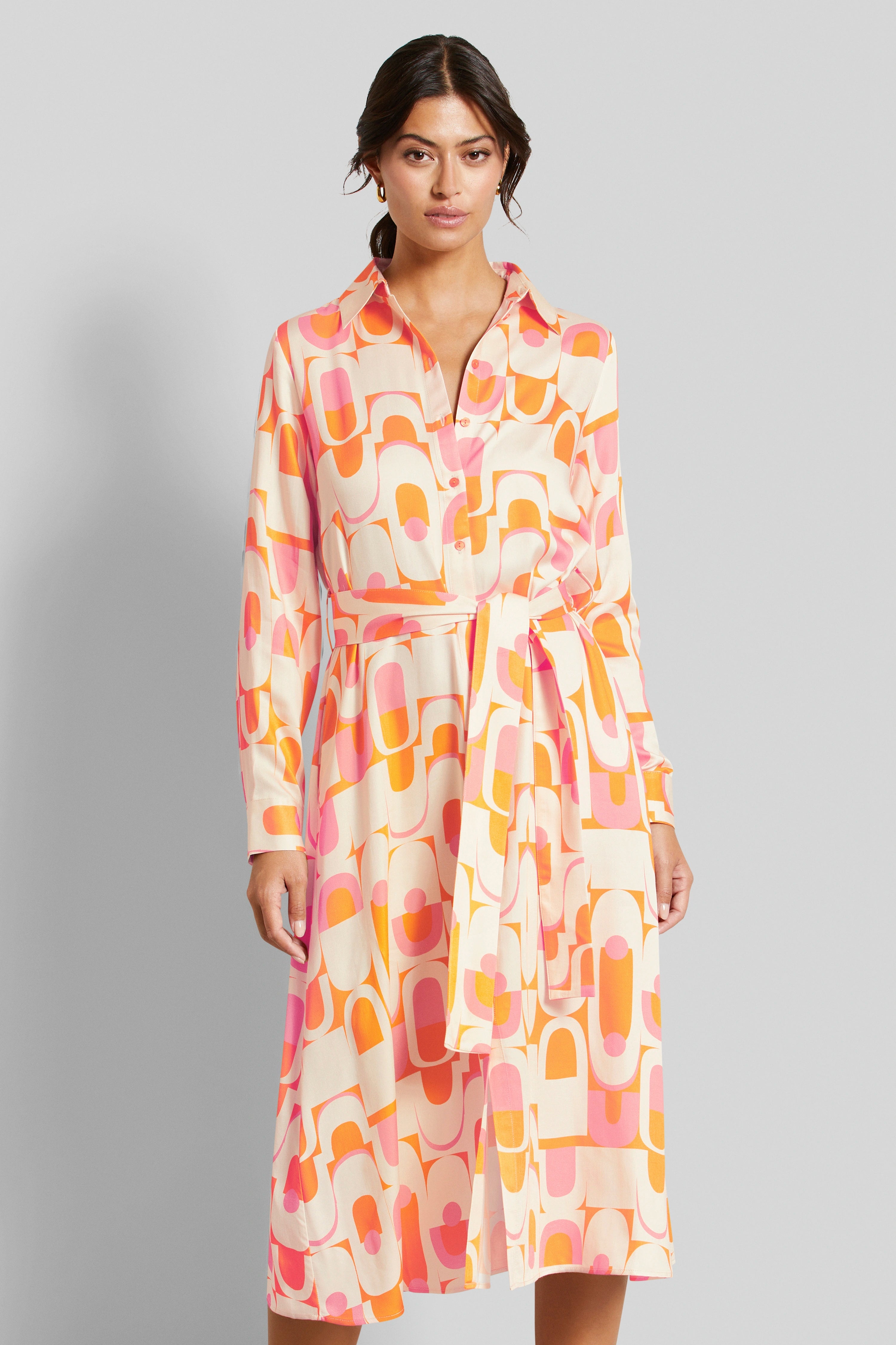 Model wearing colorful patterned shirt dress in orange and pink, standing, front view.