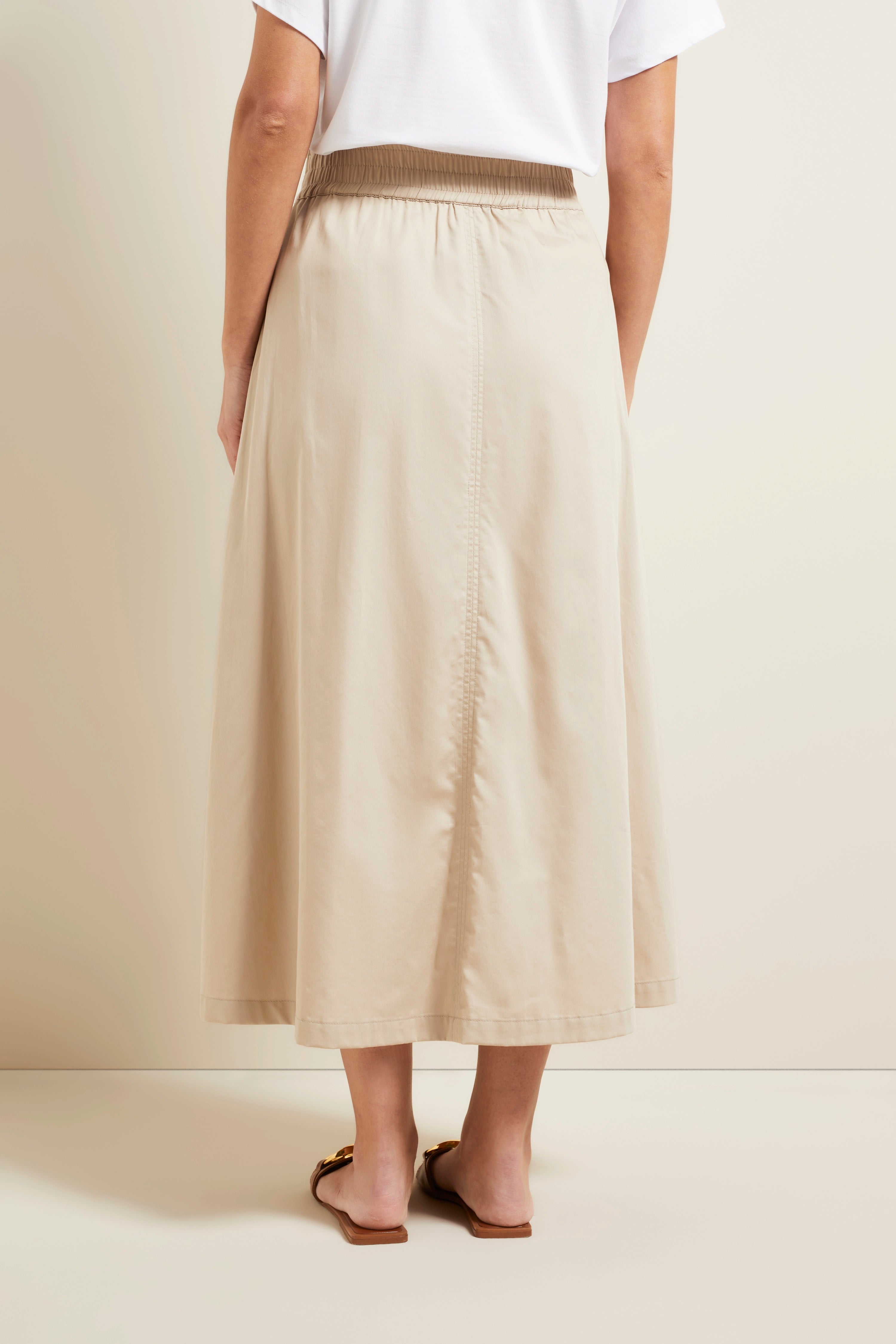Beige maxi skirt with white T-shirt, casual model photo from behind, relaxed pose, embodying bugatti's Italian elegance.