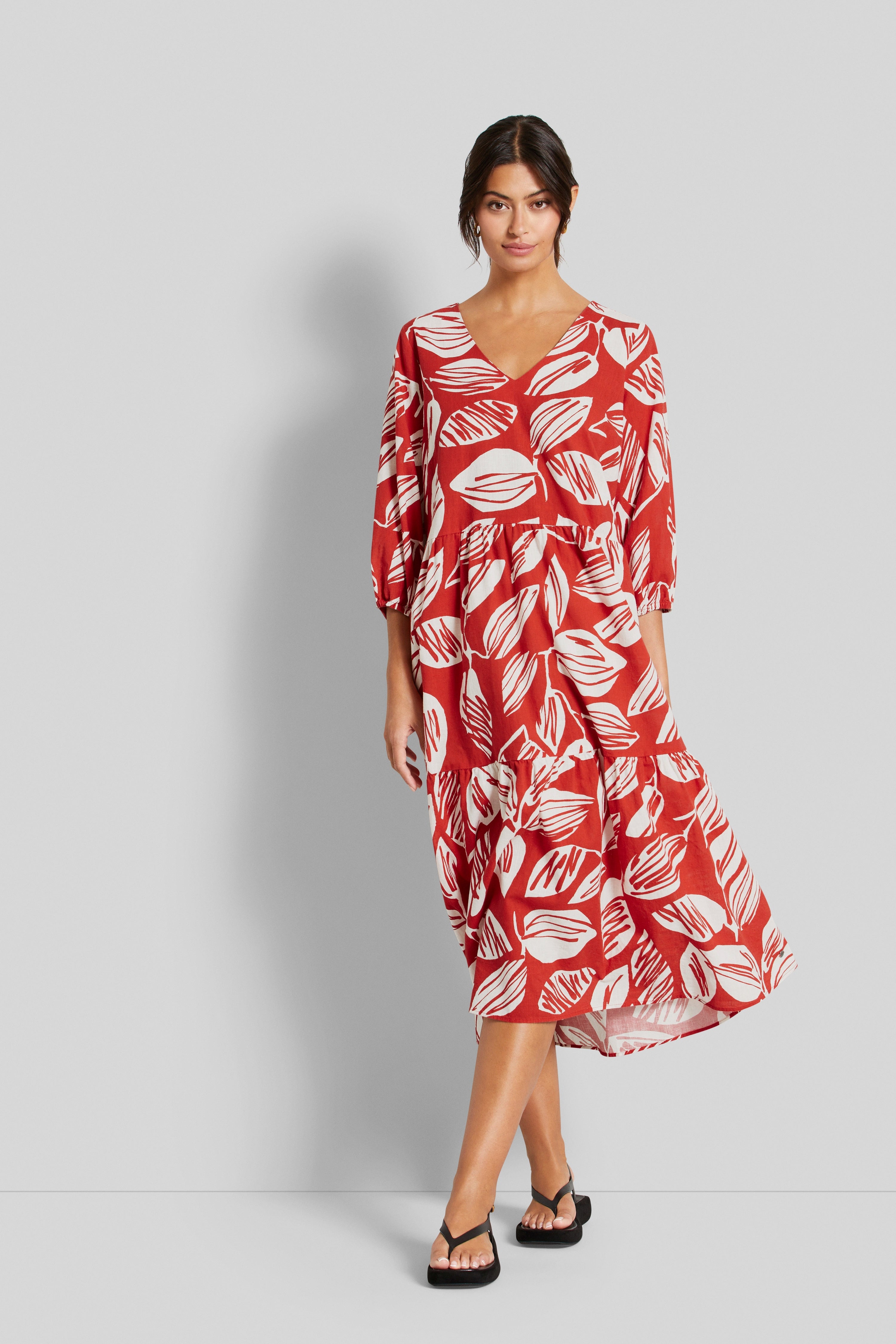Rotes Midi-Kleid mit weißem Blattmuster. Model posiert frontal mit entspanntem Ausdruck.