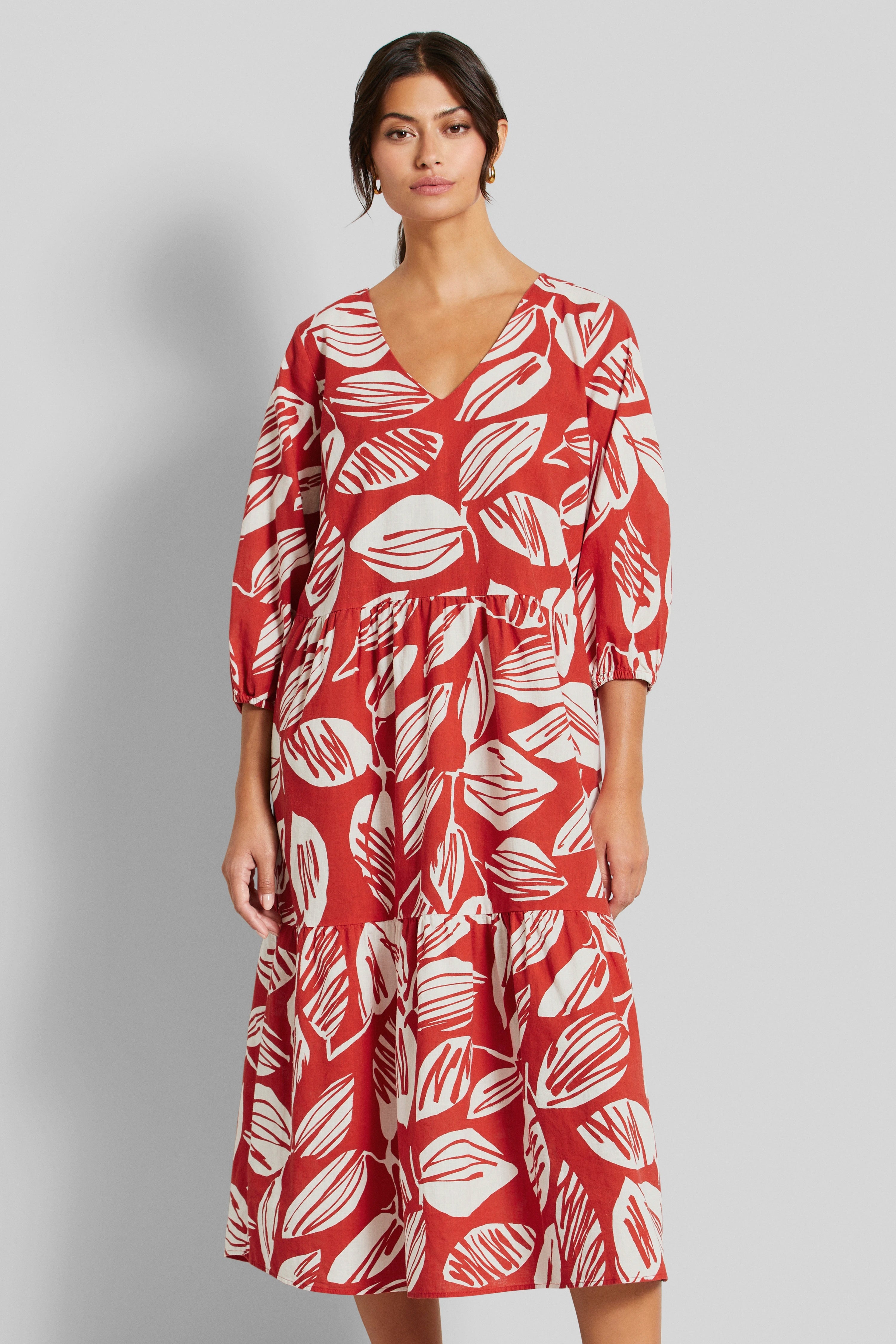 Rotes Kleid mit weißem Blattmuster, V-Ausschnitt, Modellbild, entspannte Pose.