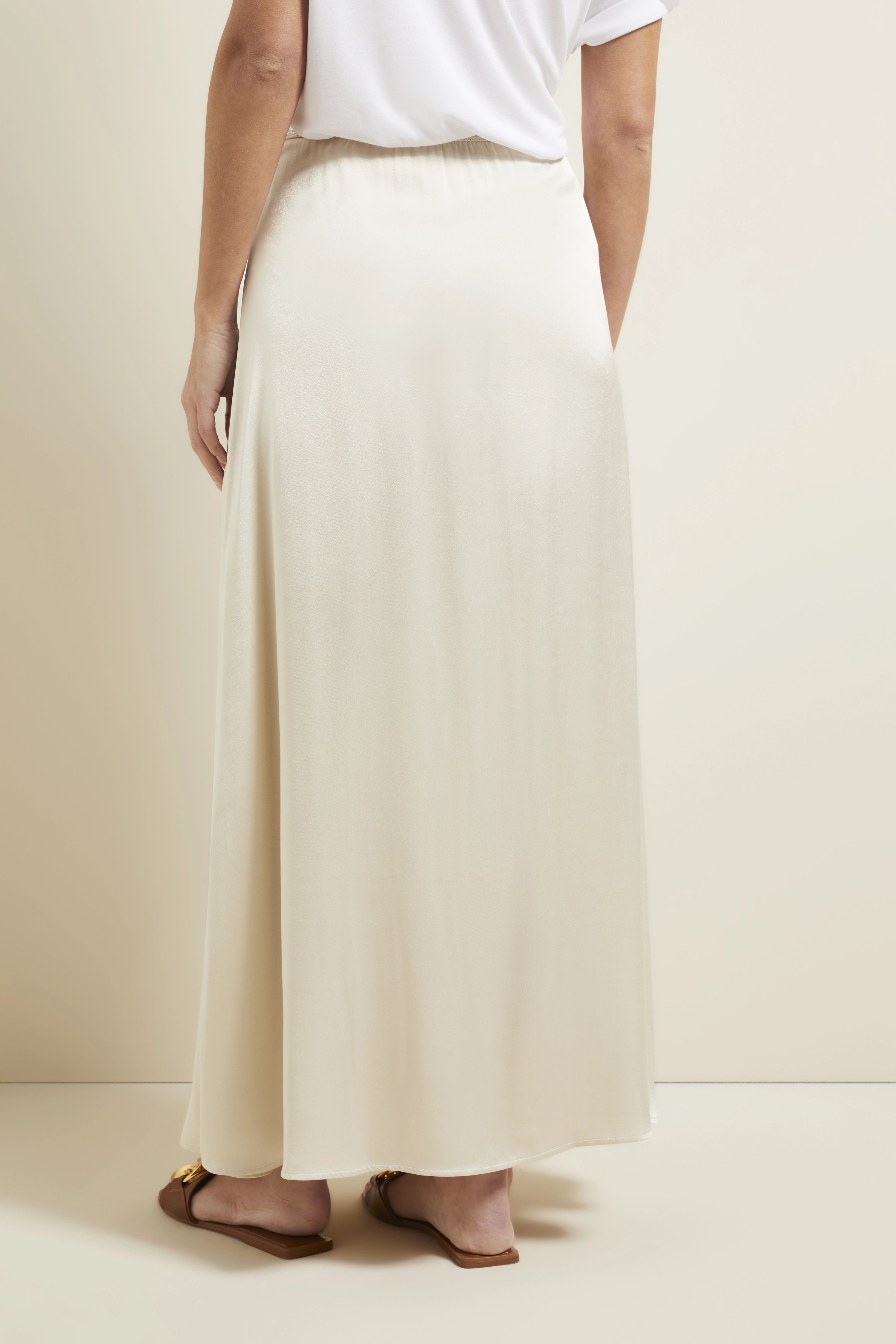 Lange crèmekleurige rok van bugatti, casual met wit shirt en sandalen. Model van achteren.