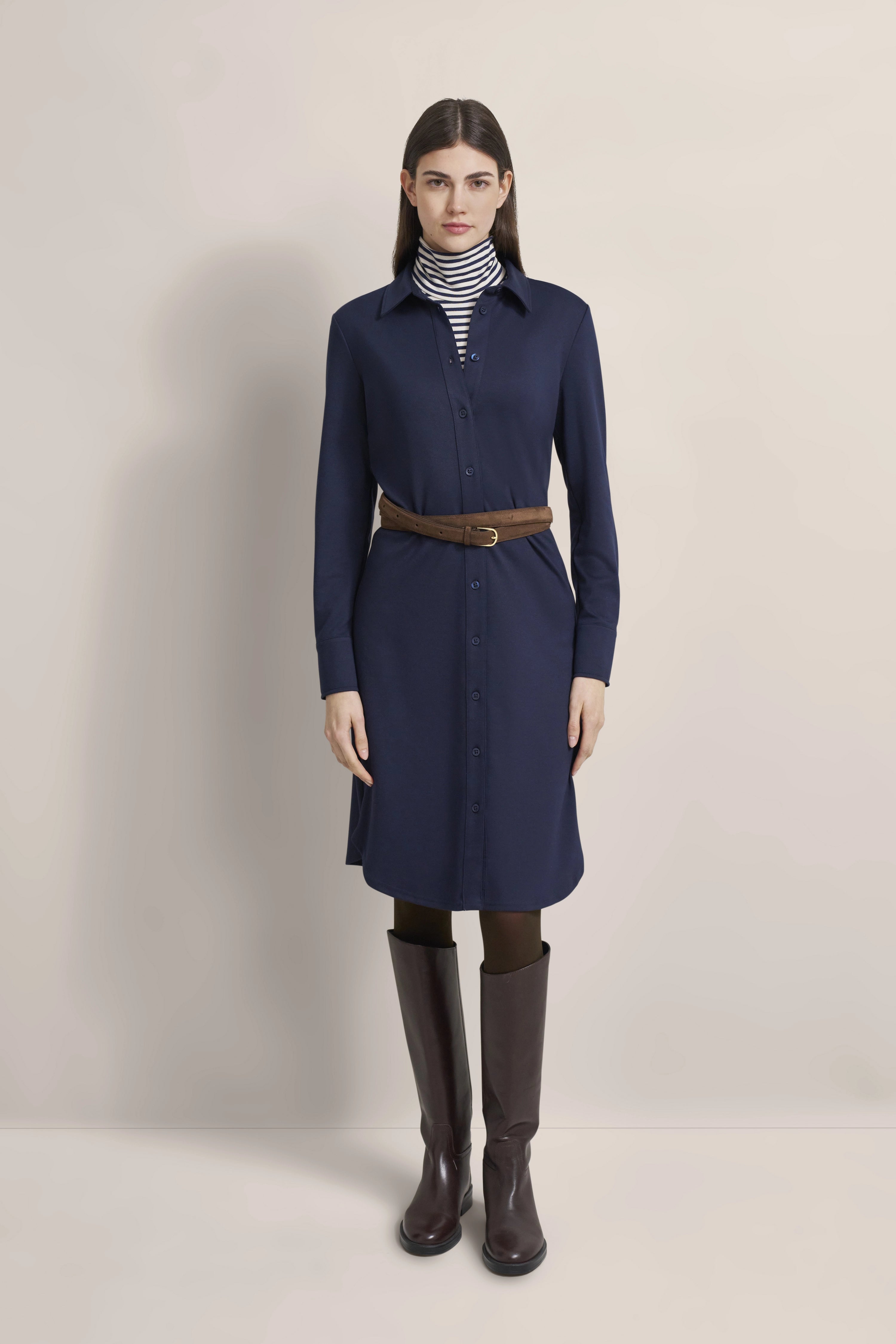 Navy shirt dress, brown belt, striped turtleneck, brown boots, model standing front.