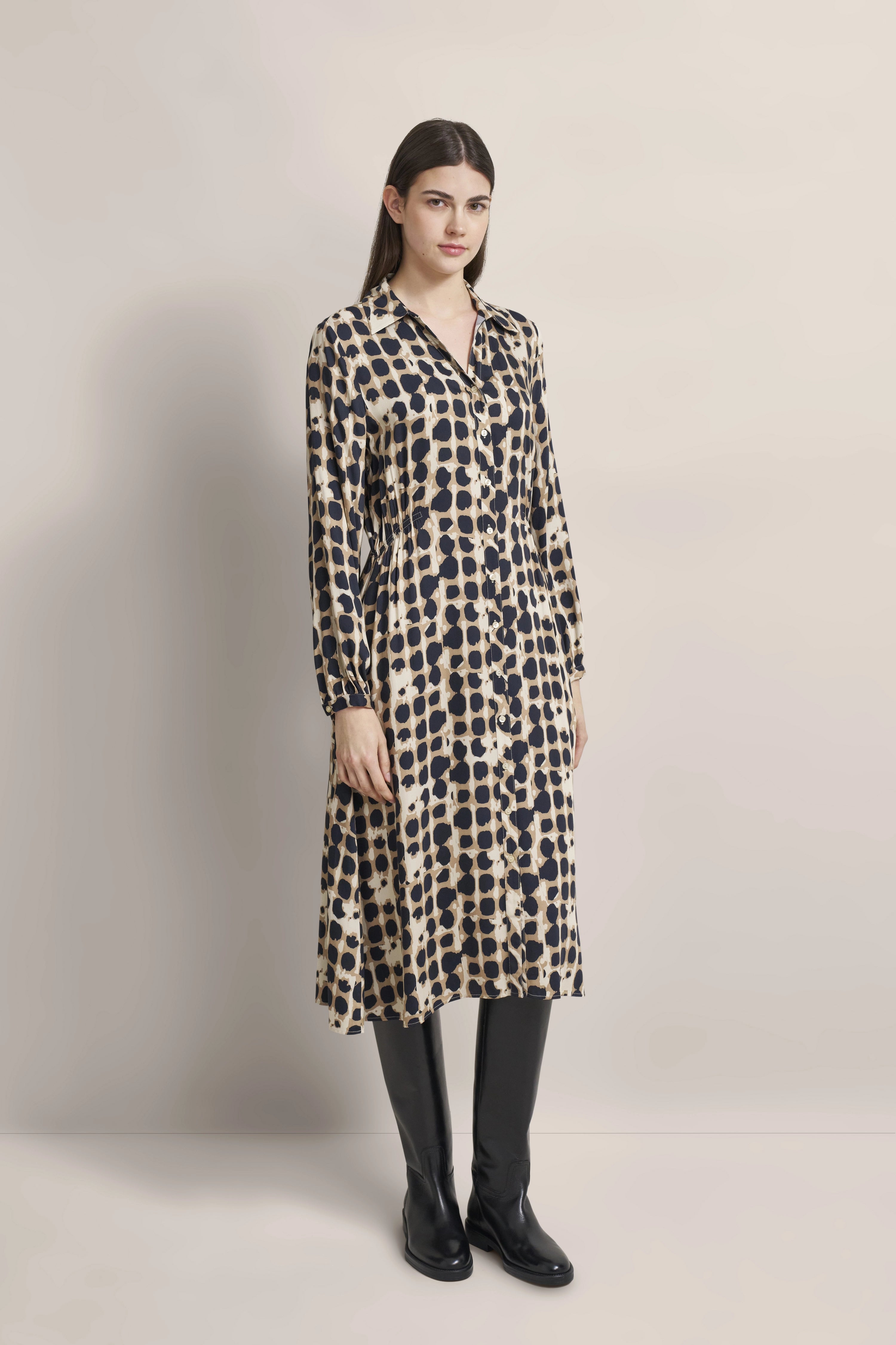 Model trägt gemustertes bugatti-Kleid in Beige-Schwarz mit langen Ärmeln, kombiniert mit schwarzen Stiefeln.