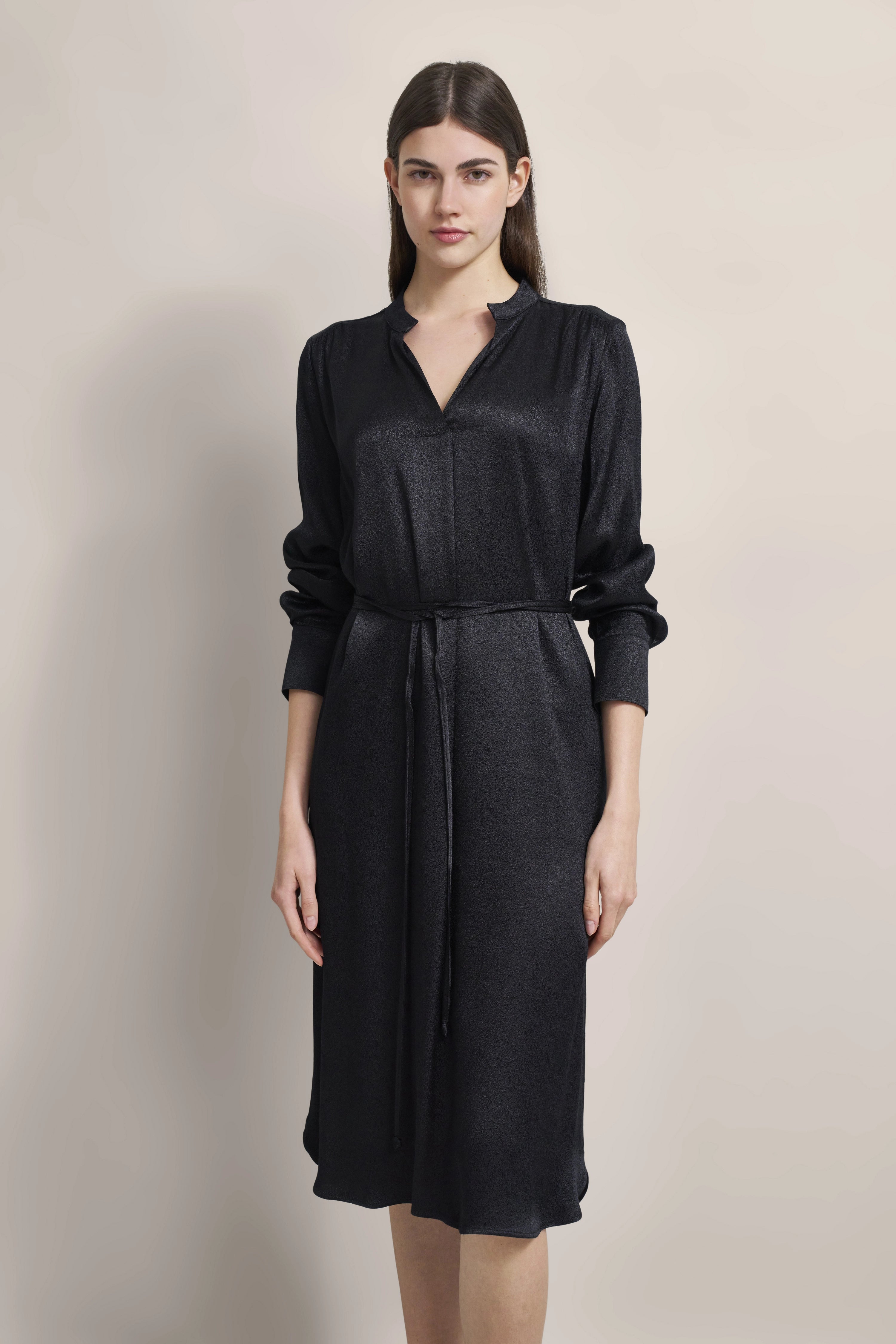 Model in black bugatti dress with V-neck and waist belt, relaxed pose.