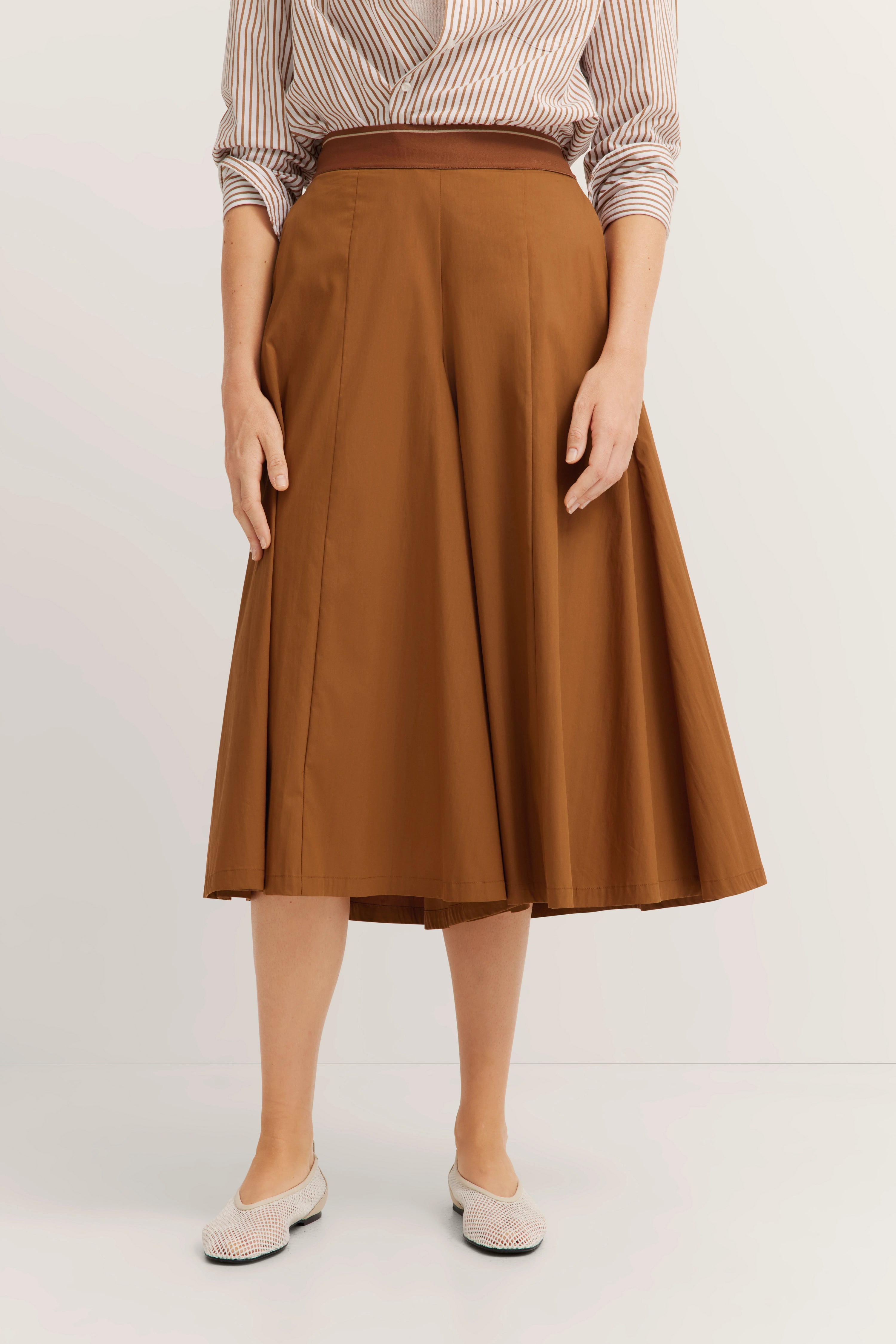 Brauner A-Linien-Rock mit gestreifter Bluse, legeres Modelbild, entspannte Pose.