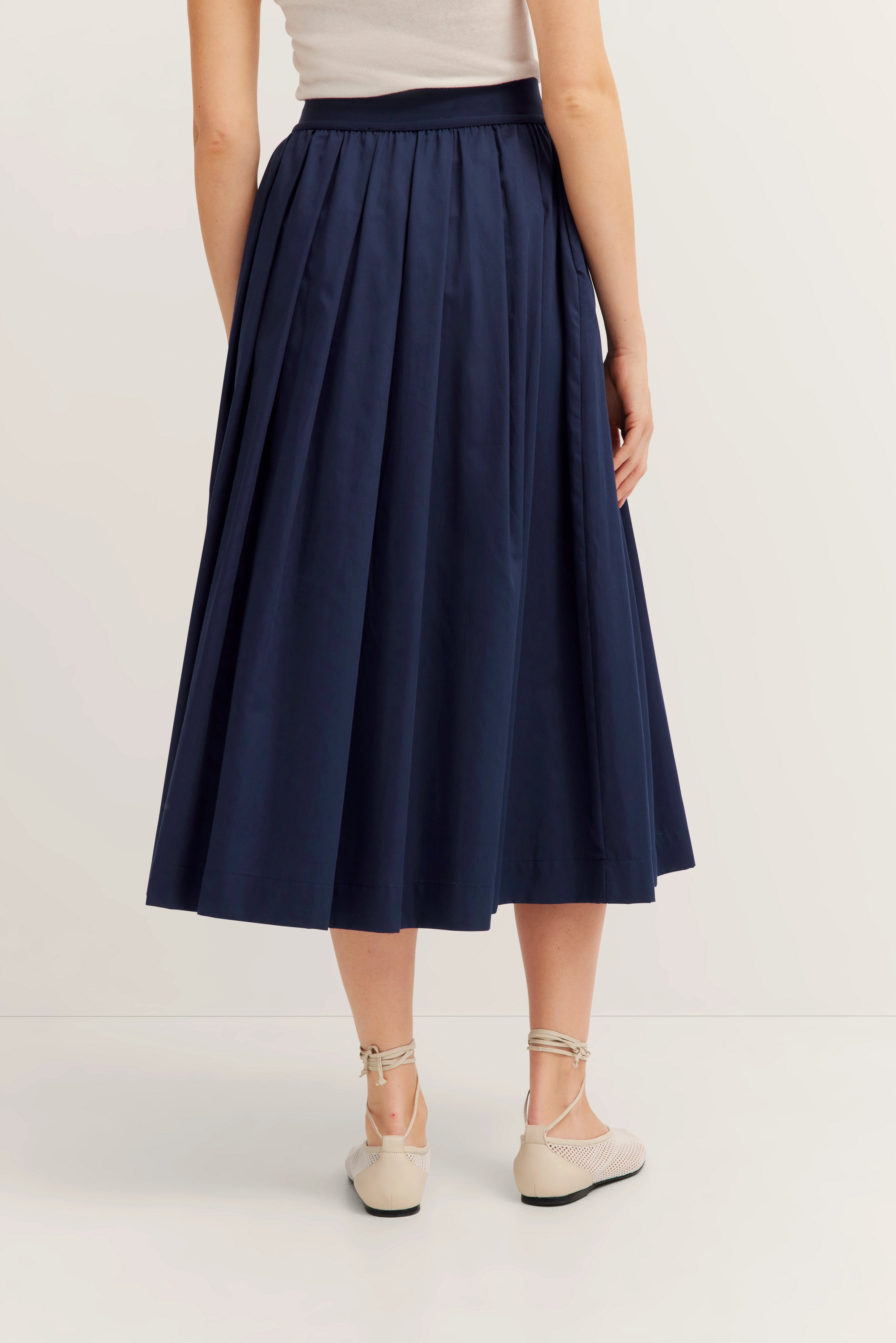 Donkerblauwe, knielange plooirok, casual model van achteren, met crèmekleurige ballerina's.