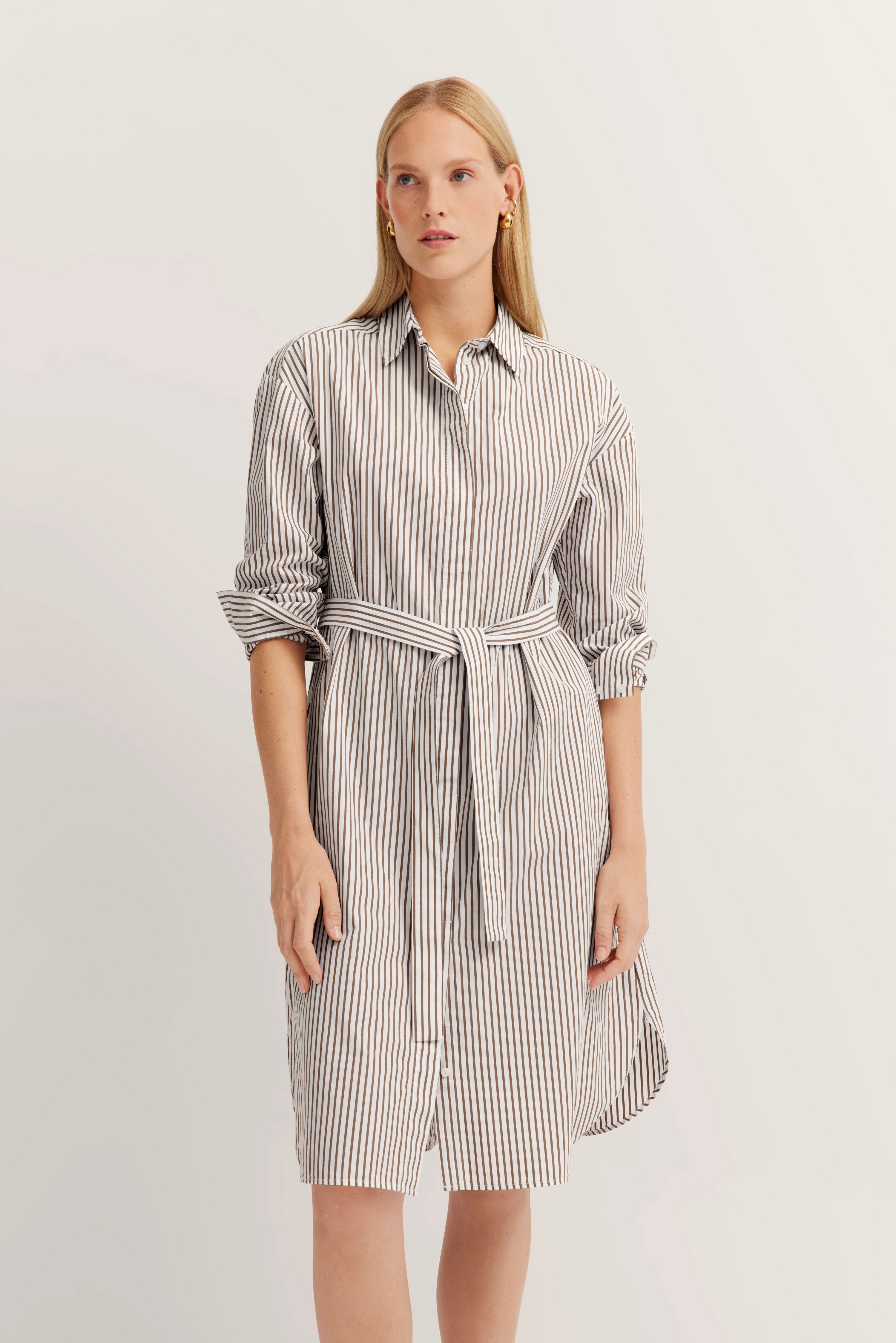 White striped shirt dress with belt, model standing relaxed. bugatti style and elegance.