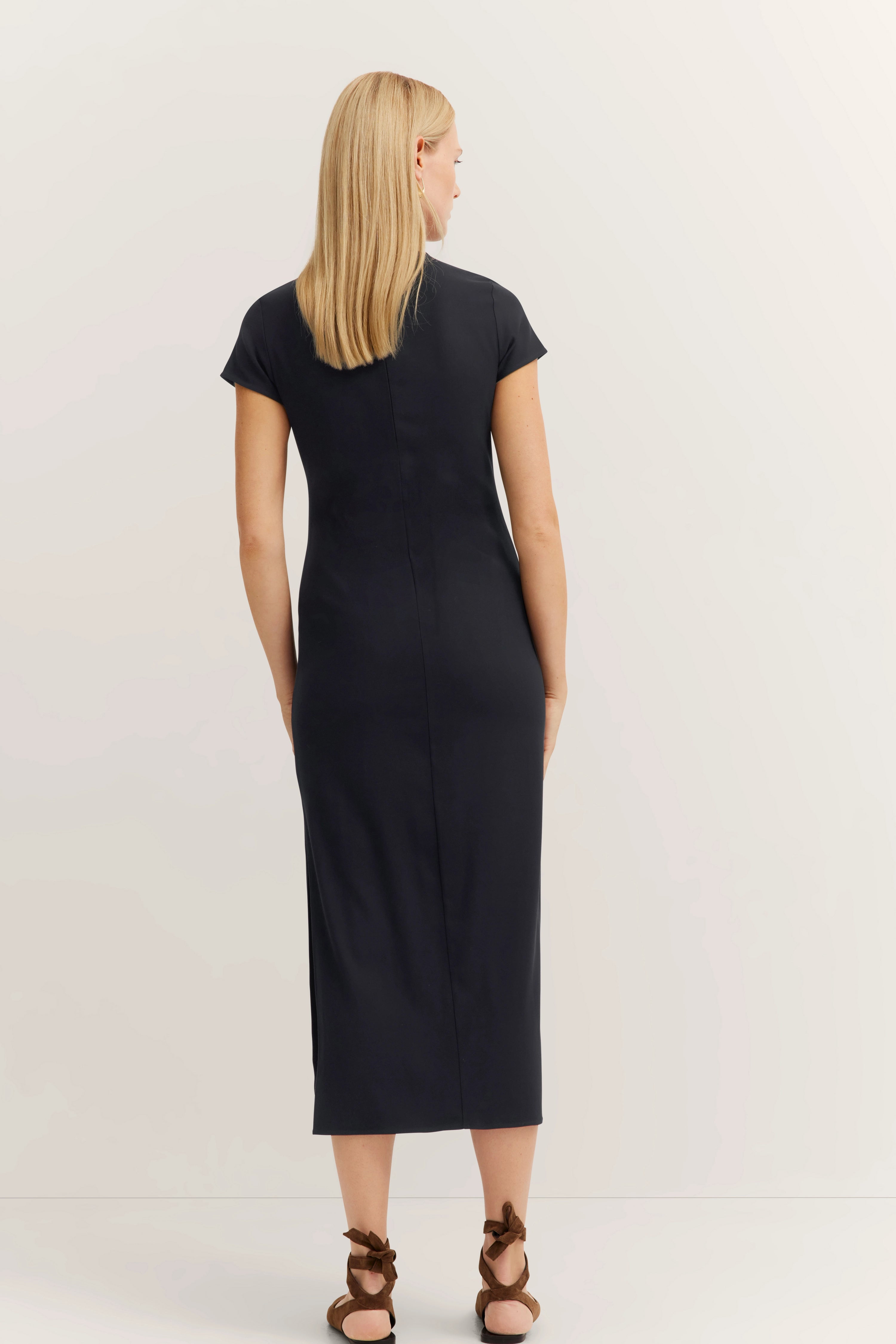 Model in navy bugatti knee-length dress, back view, simple design, brown sandals.