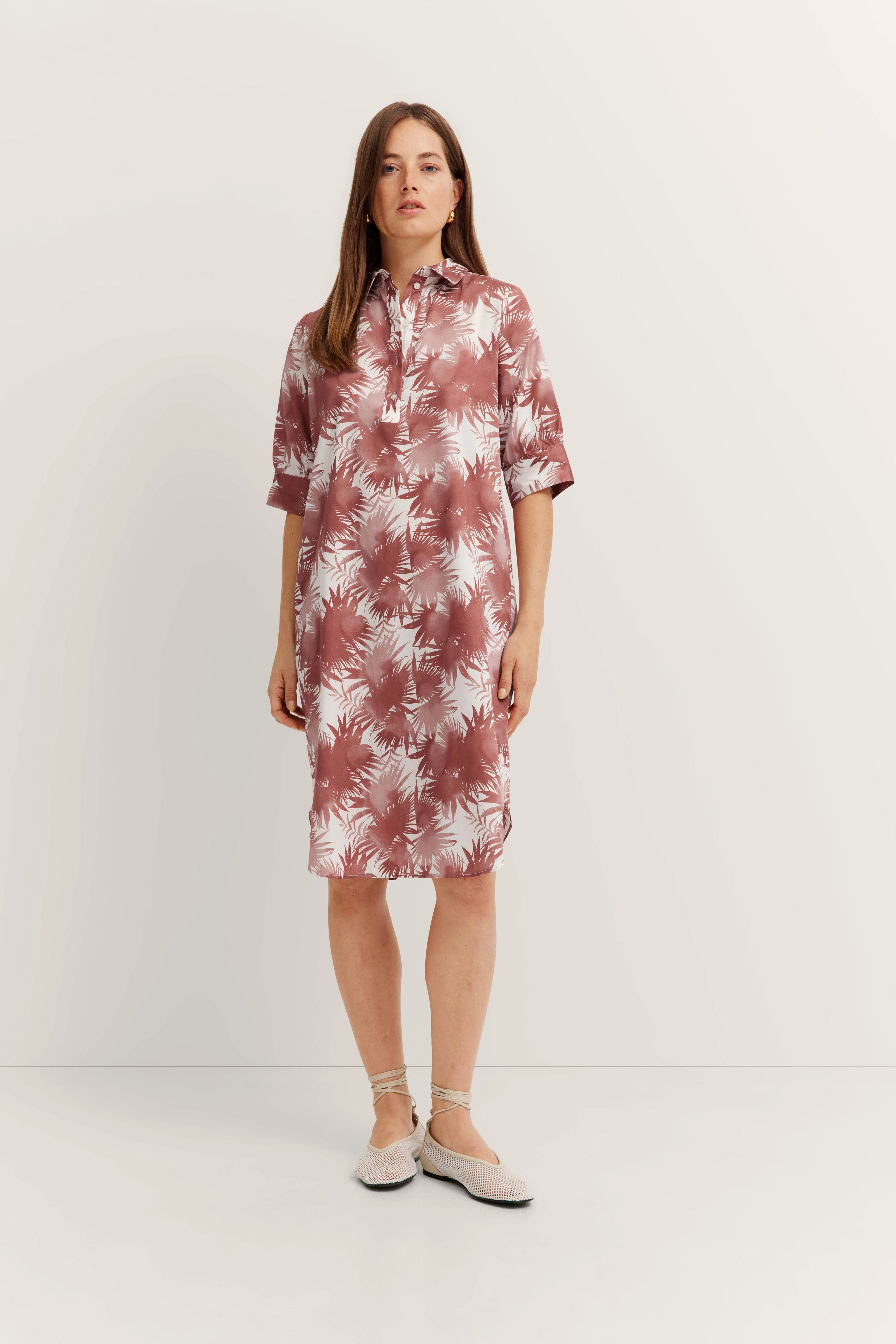 Damenkleid mit rosa-weißem Palmenmuster, kurze Ärmel, Modelbild stehend, entspannte Pose.