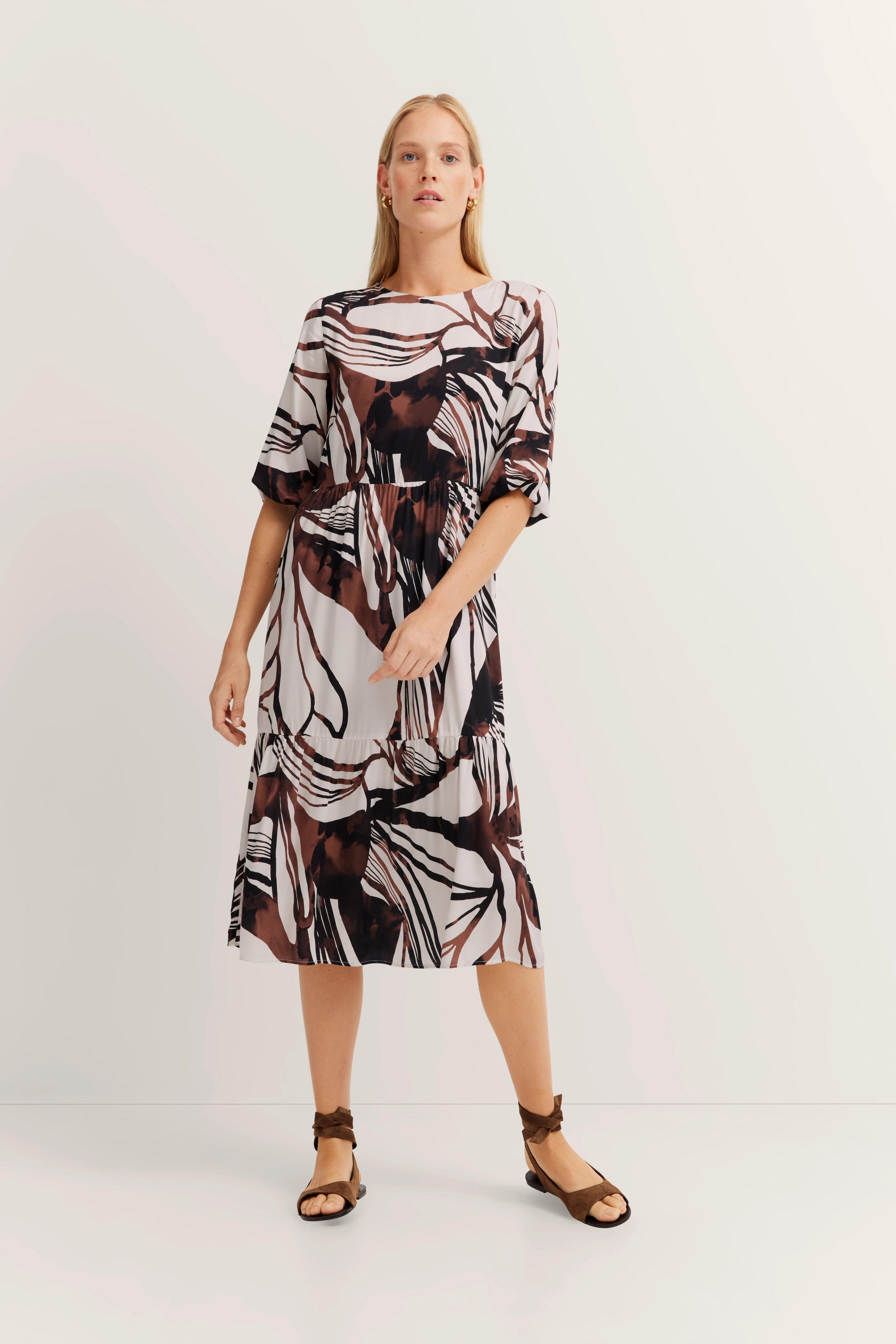 Model in gemustertem bugatti Kleid in Braun und Weiß mit 3/4-Ärmeln, locker stehend.