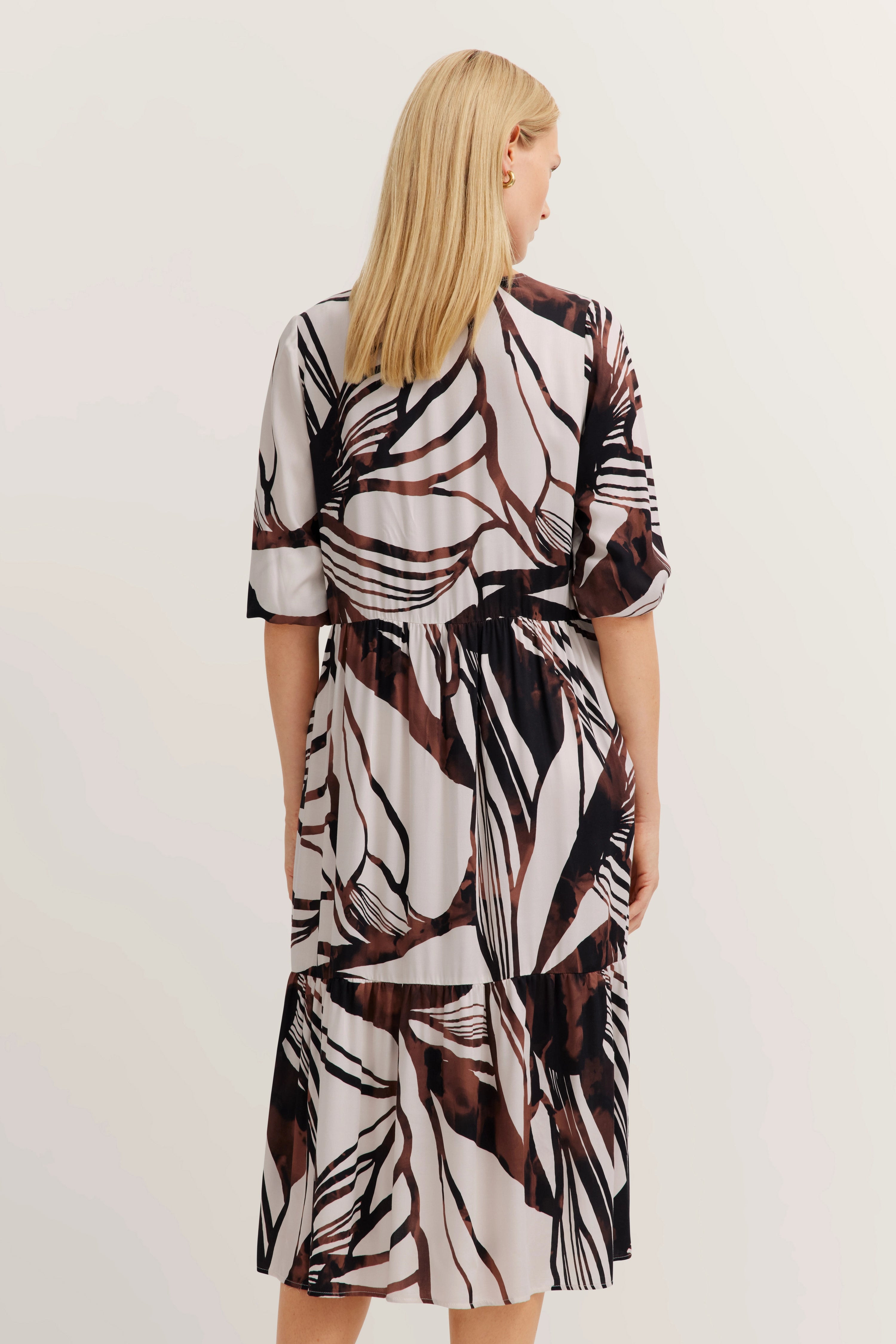 Model trägt geblümtes Kleid in Braun und Weiß, Rückansicht, lässiges Posing, bugatti Stil.