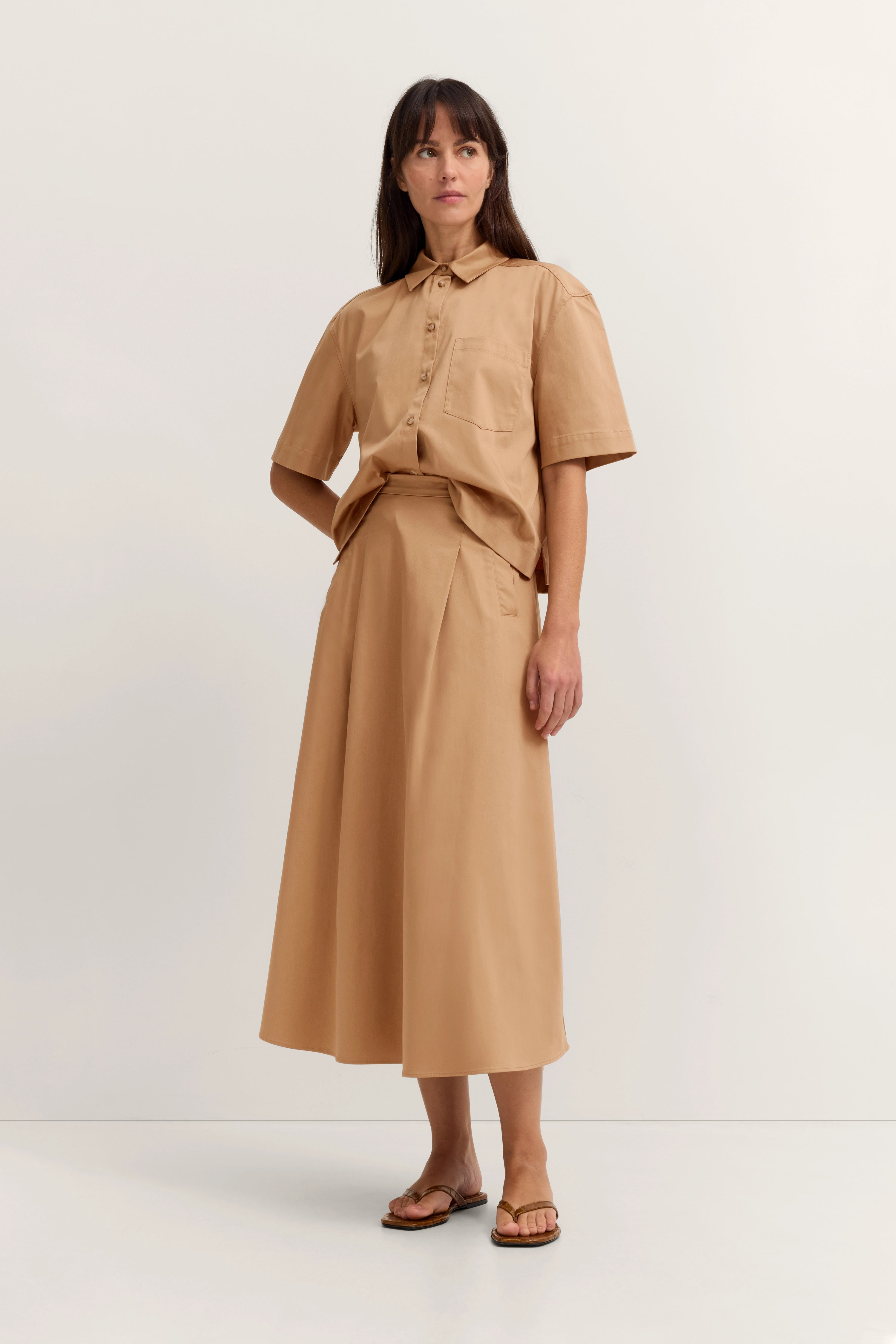 Beiges Model-Outfit mit Hemd und Midirock, legeres Posing, stilvoll und zeitlos von bugatti inspiriert.