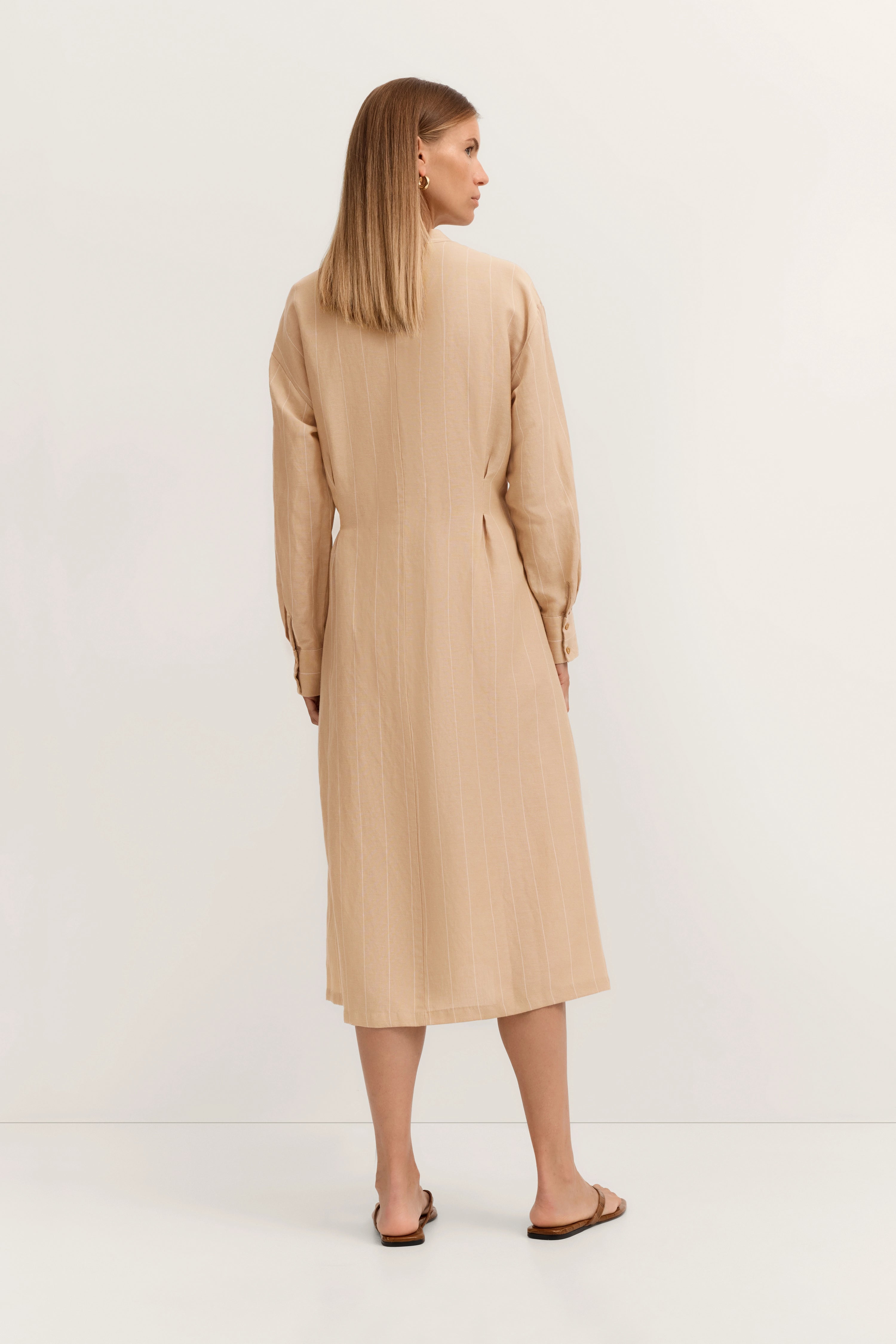 Beiges, langes Kleid mit feinen Streifen, Model von hinten, entspanntes Posing.