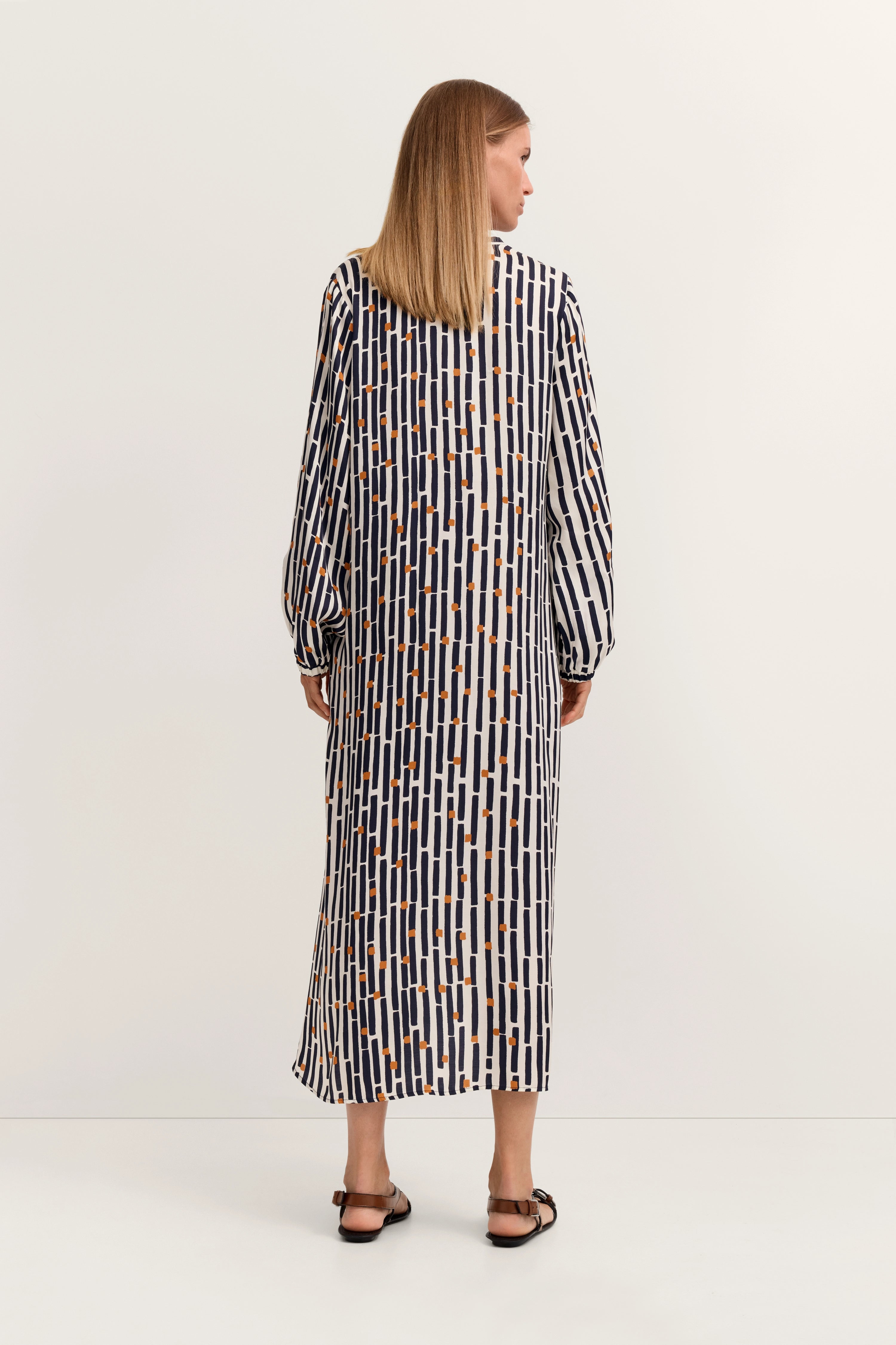 Langes gemustertes Kleid in Blau und Weiß, Model von hinten, lässige Pose, bugatti Stil.