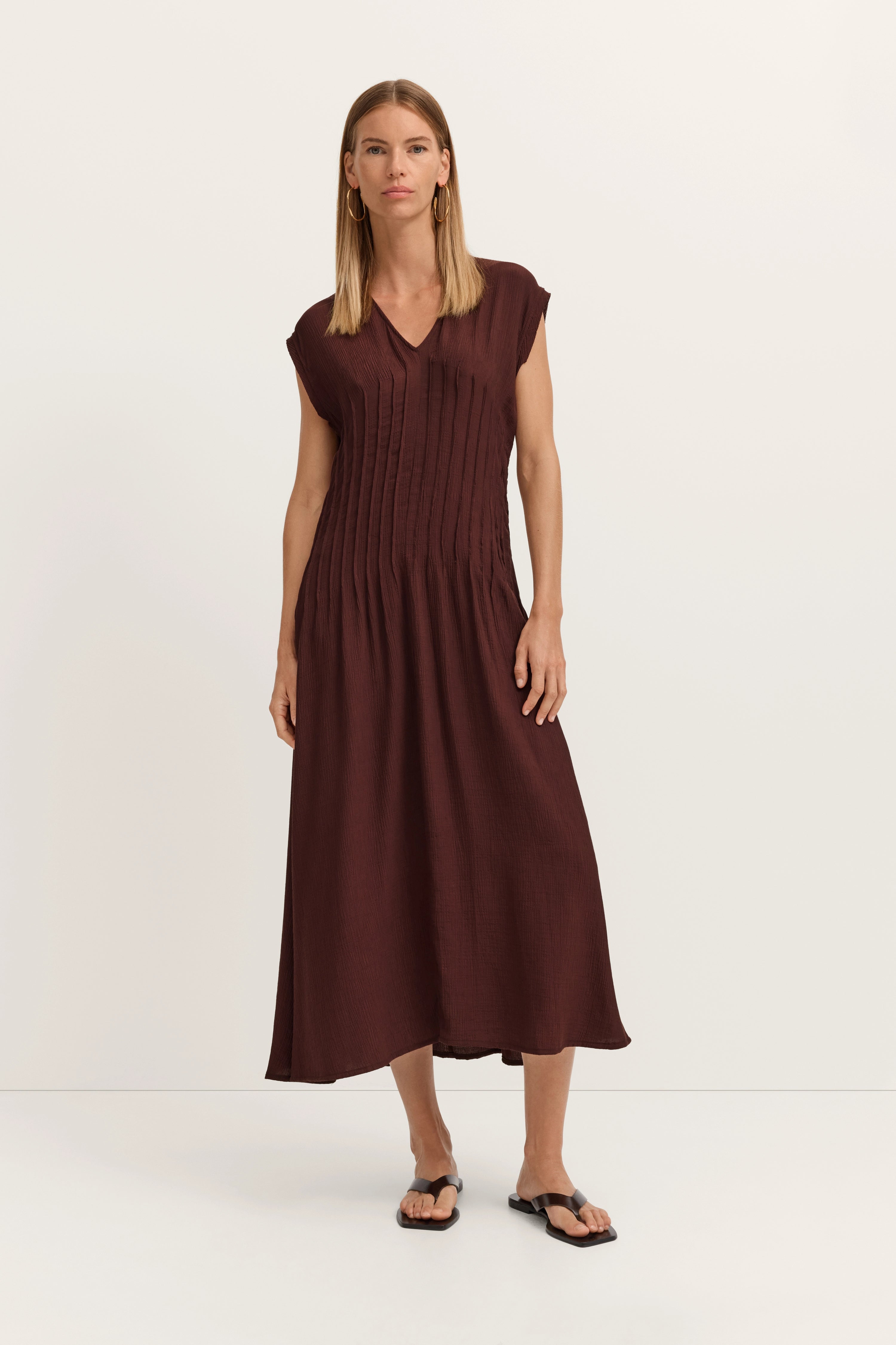 Model in langem, braunem Kleid mit V-Ausschnitt, gerade stehend.