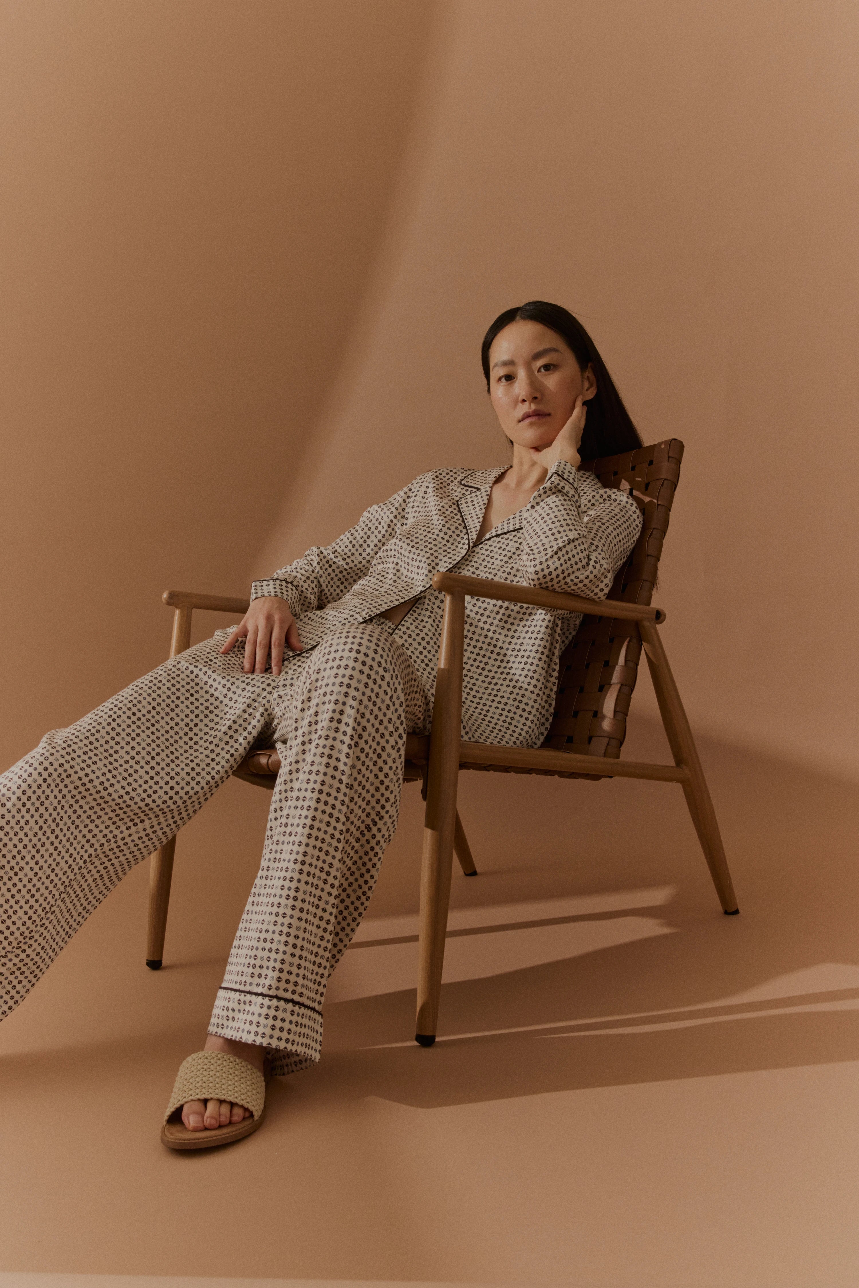 Model in gemustertem, beigem Pyjama sitzt lässig im Stuhl, entspannter Look für bugatti.