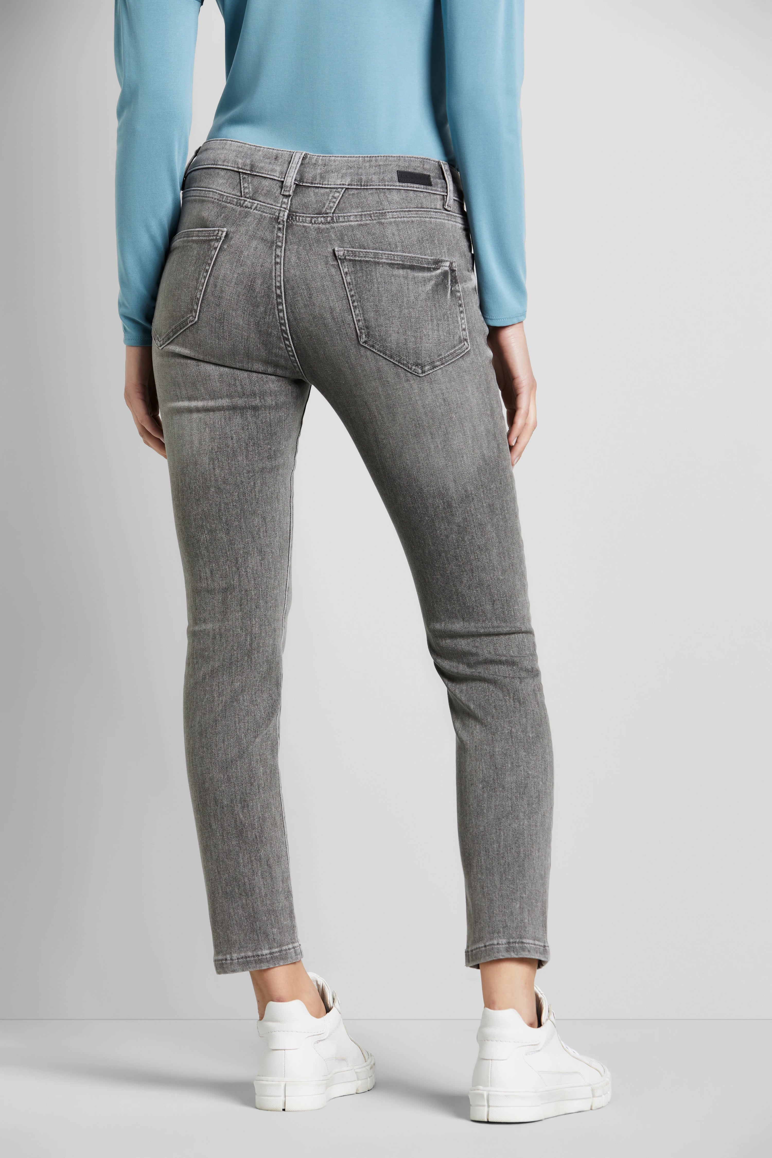 Graue Jeans und blaues Oberteil, Model von hinten, weiße Sneaker, entspannte Pose.