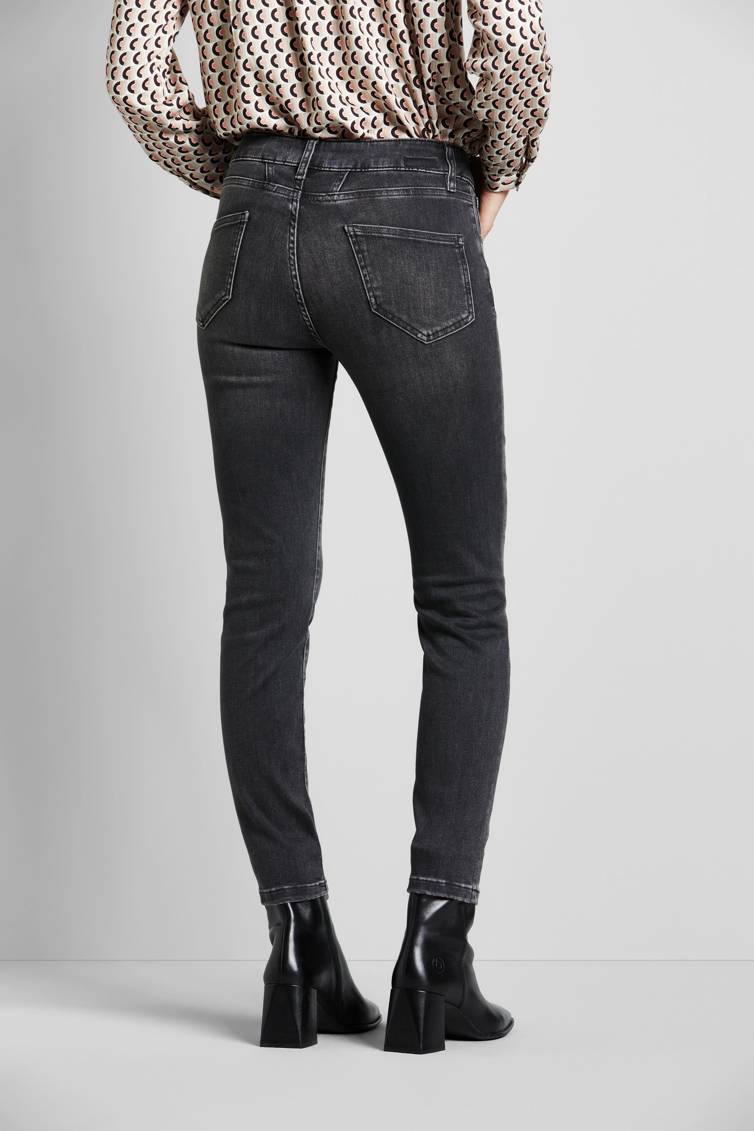 Schwarze Skinny-Jeans und gemusterte Bluse, Modelansicht von hinten, schwarze Stiefel.