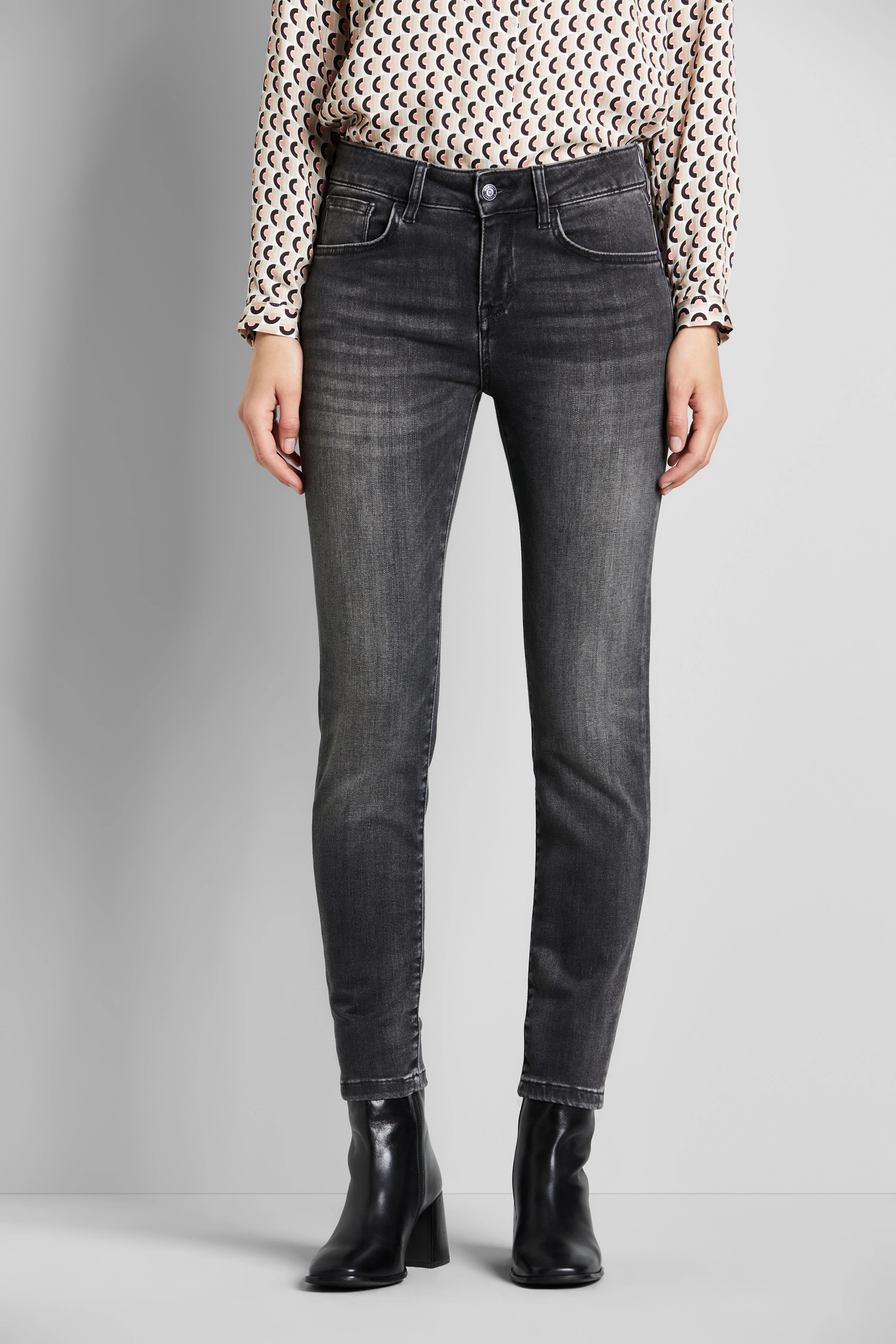 Dark jeans and patterned blouse, model standing, black ankle boots.