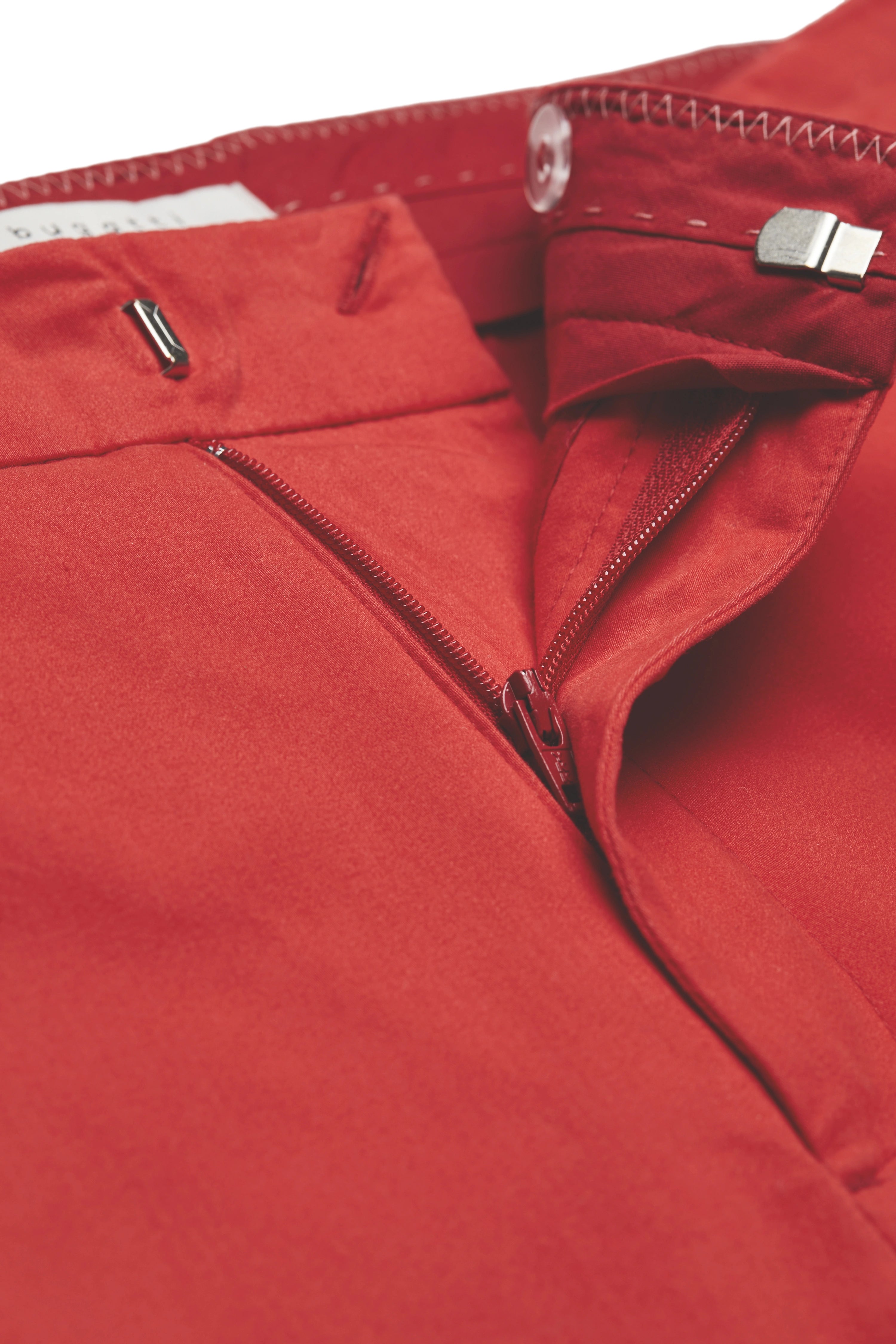 Rode bugatti-broek, close-up met rits en knoop, toont detail en kwaliteit.