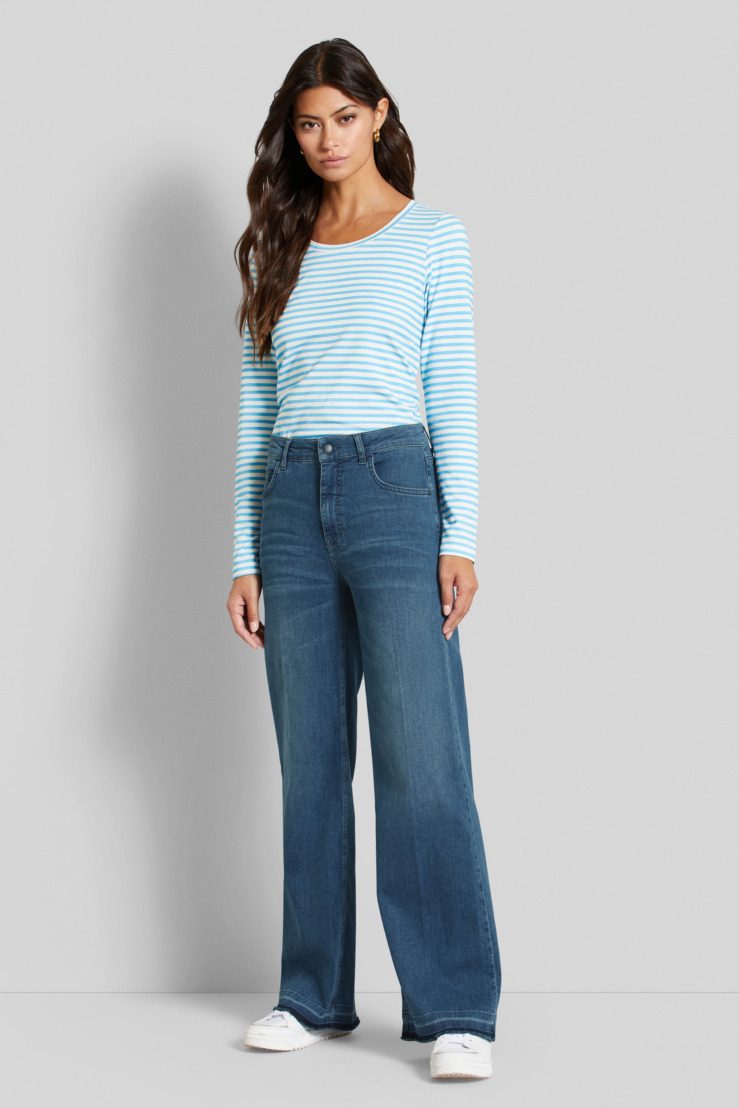 Model mit blau-weiß gestreiftem Langarmshirt und blauer Jeans, stehend, legeres Posing.