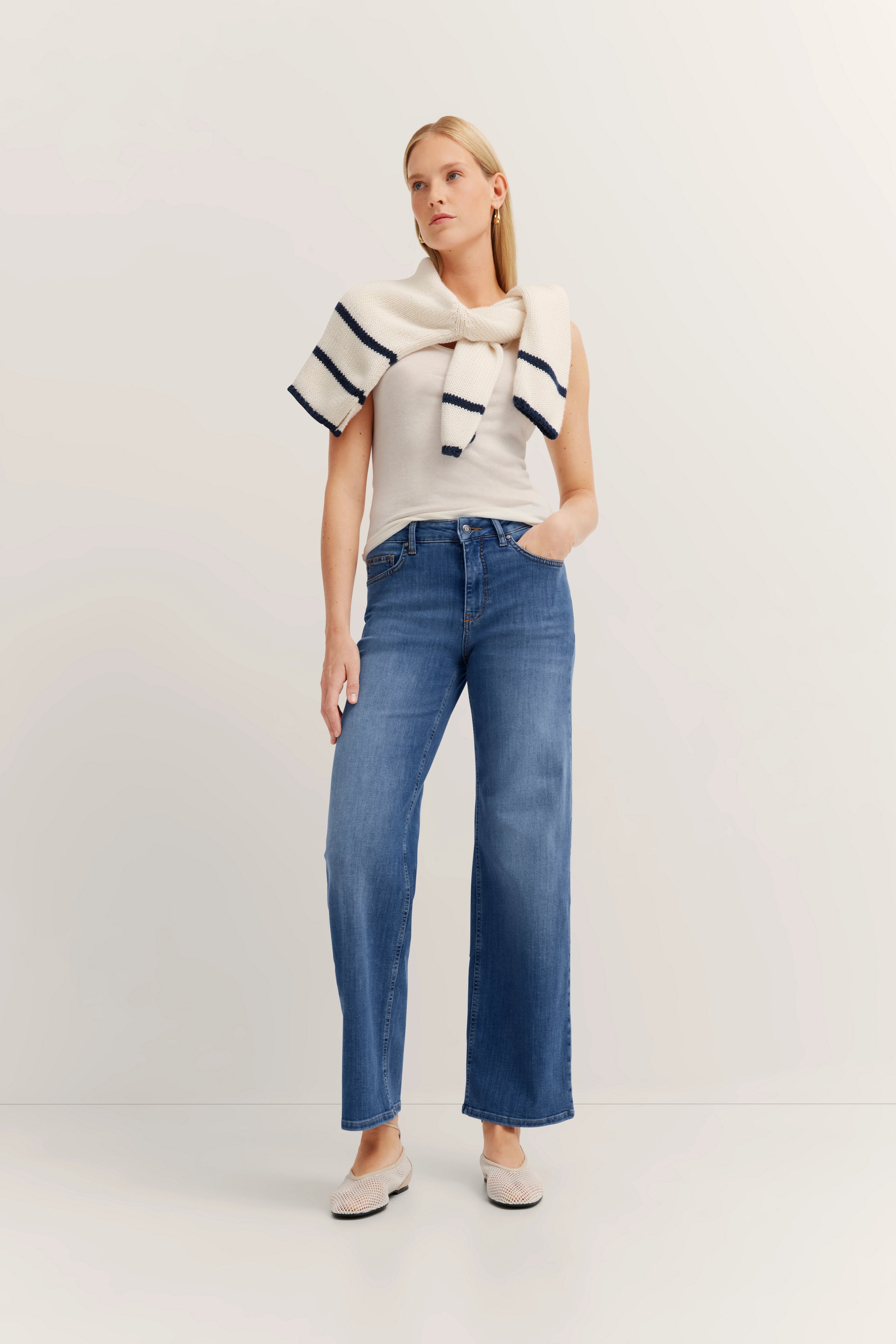 Model in jeans, wit top, trui over schouders
