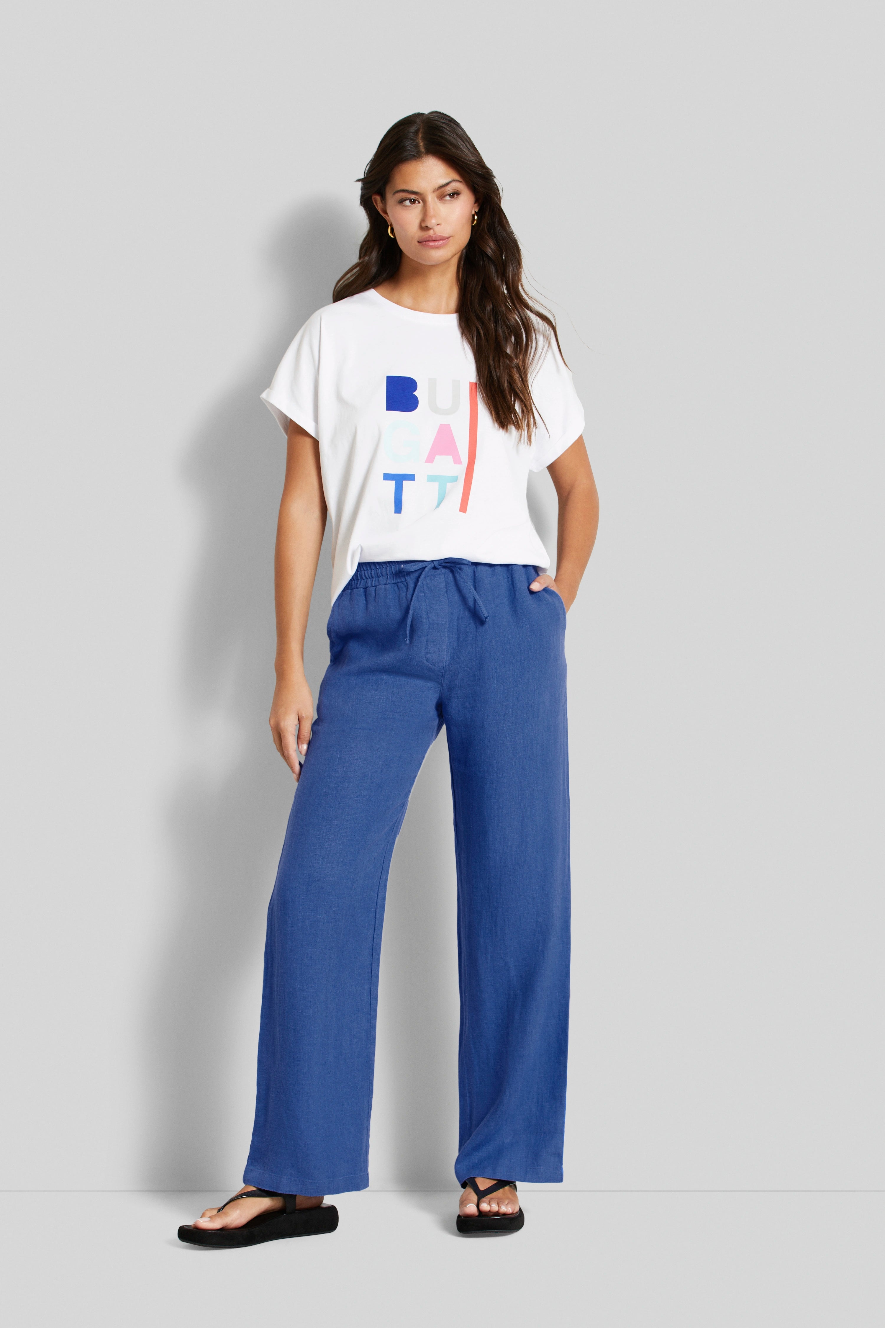 Legerbild: Weißes Shirt, blaue Hose von bugatti, lässig mit Händen in Taschen, schwarze Sandalen.