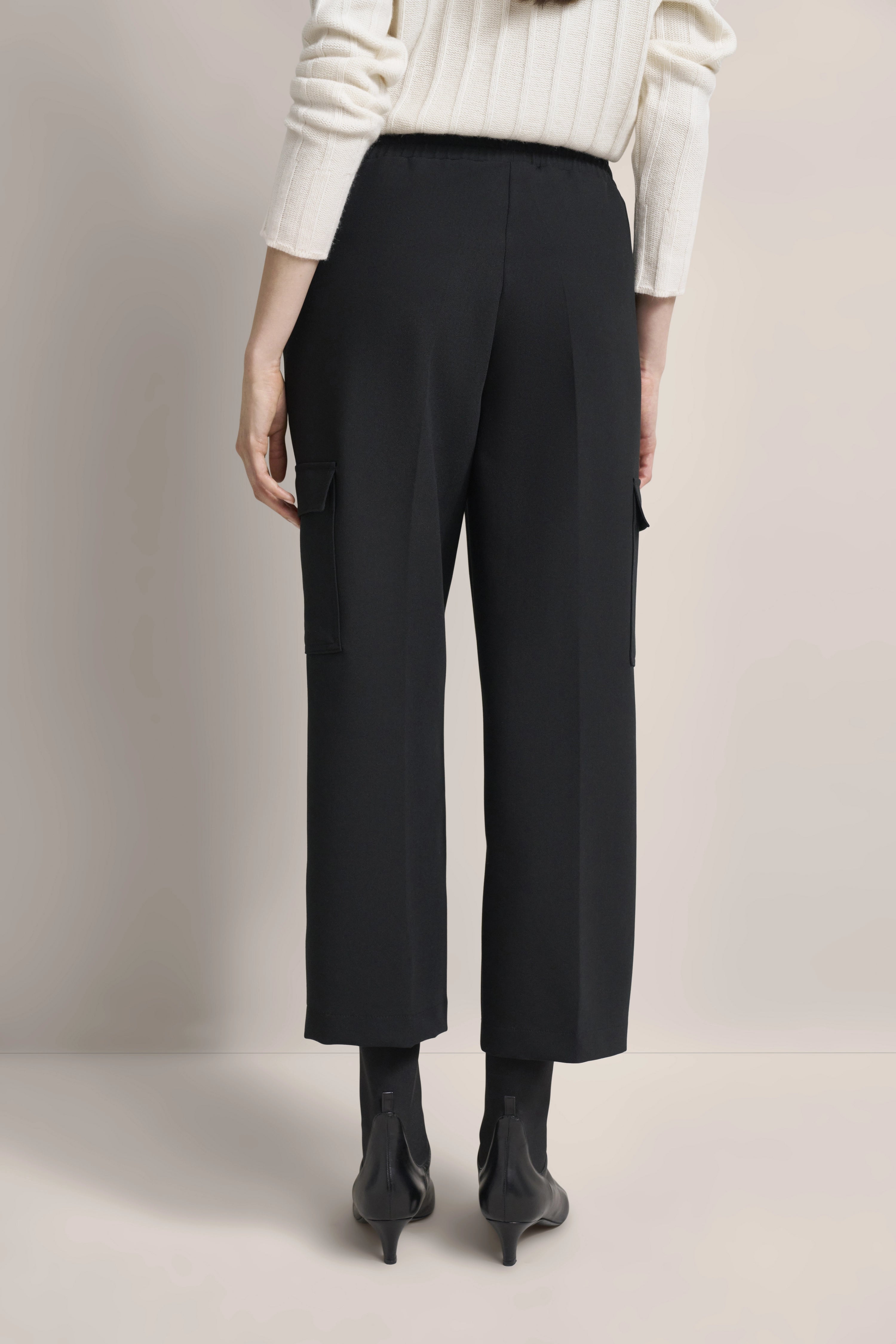 Weiße Rippenpullover mit schwarzer Hose, Modelbild, lässige Rückansicht.