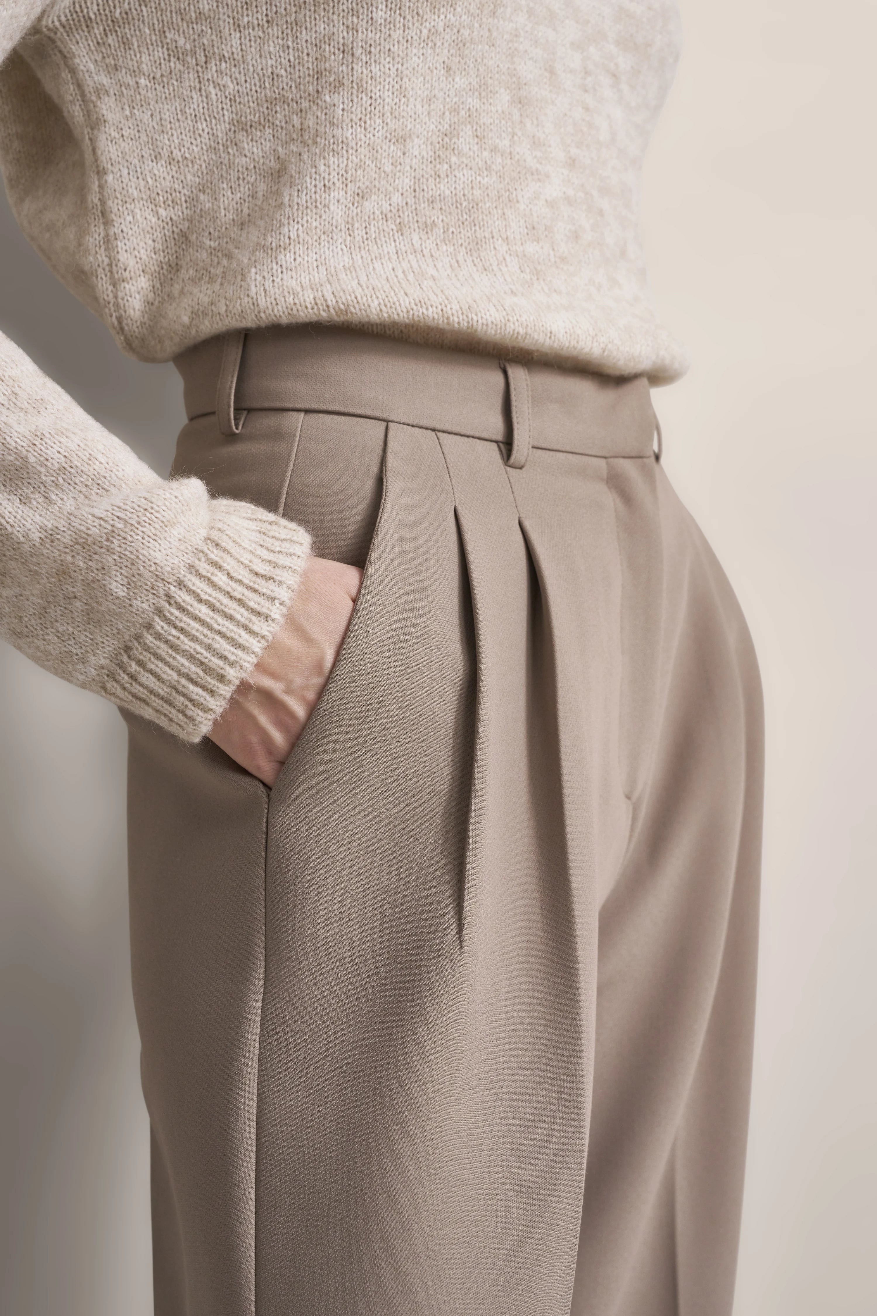 Beiger Pullover mit beiger Hose, legeres Büstenbild, Hand in Hosentasche.