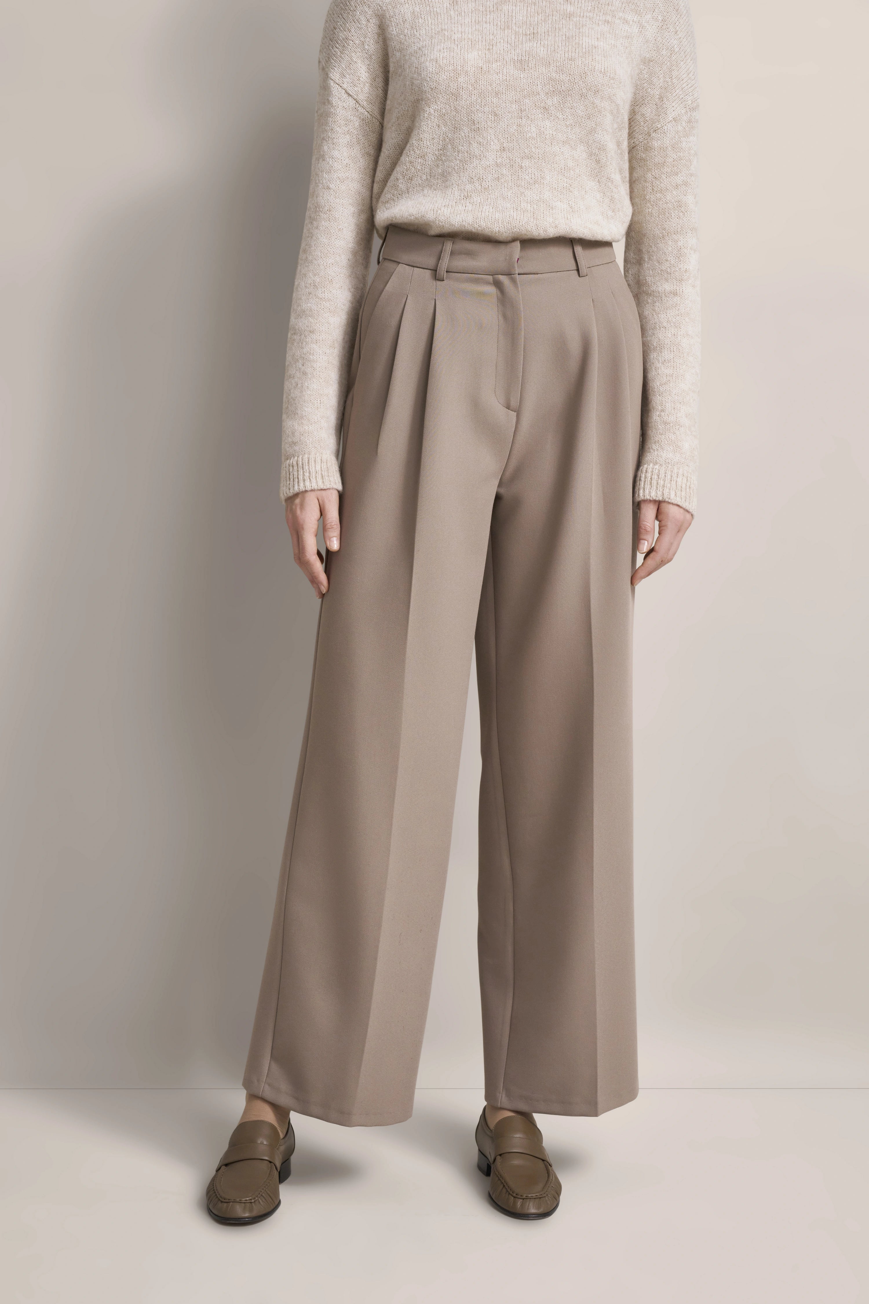 Beiges Outfit mit Strickpullover und weiten Hosen. Legerbild ohne Posing.