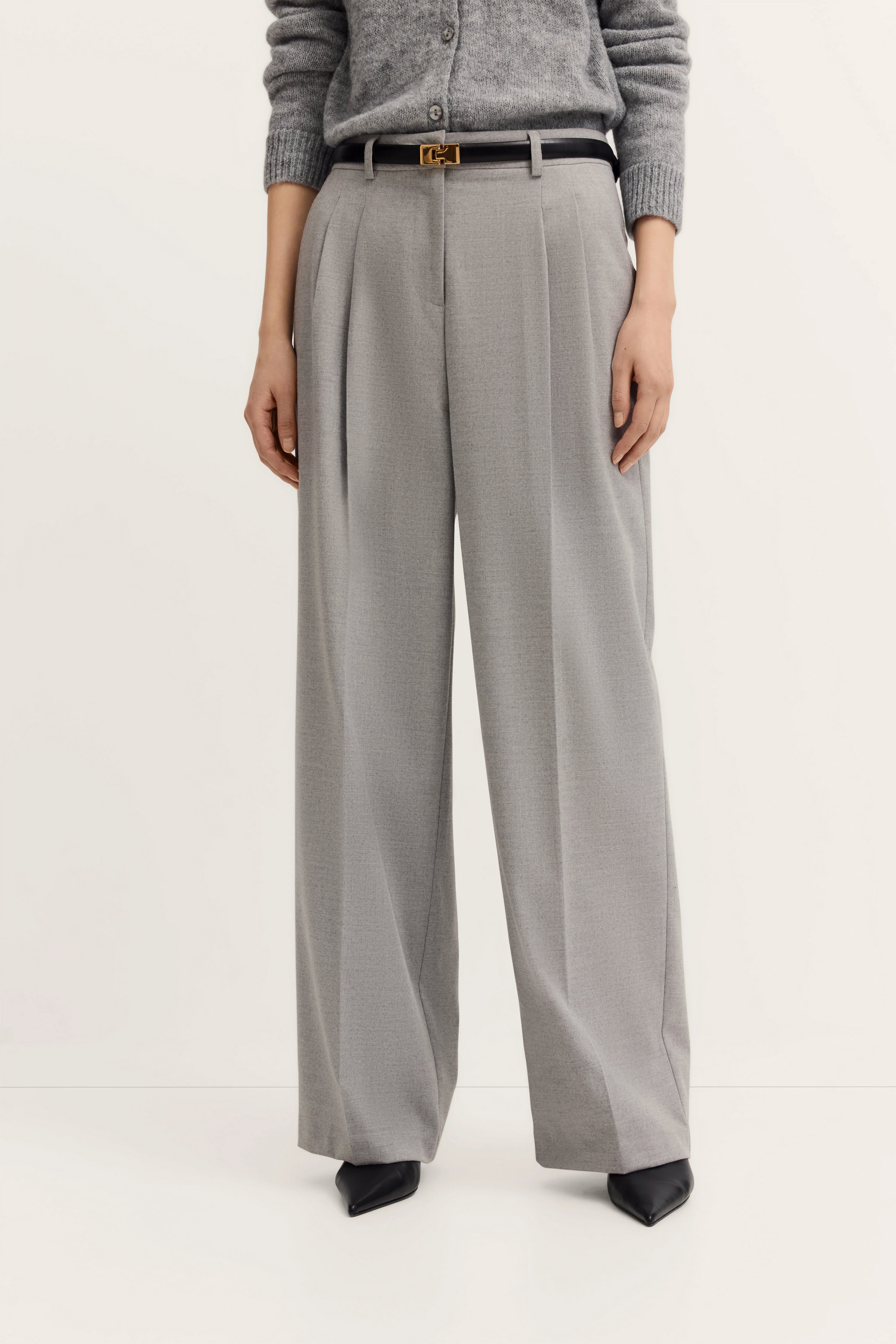 Gray wide-leg trousers with pleats, black belt, model partially shown, black shoes.