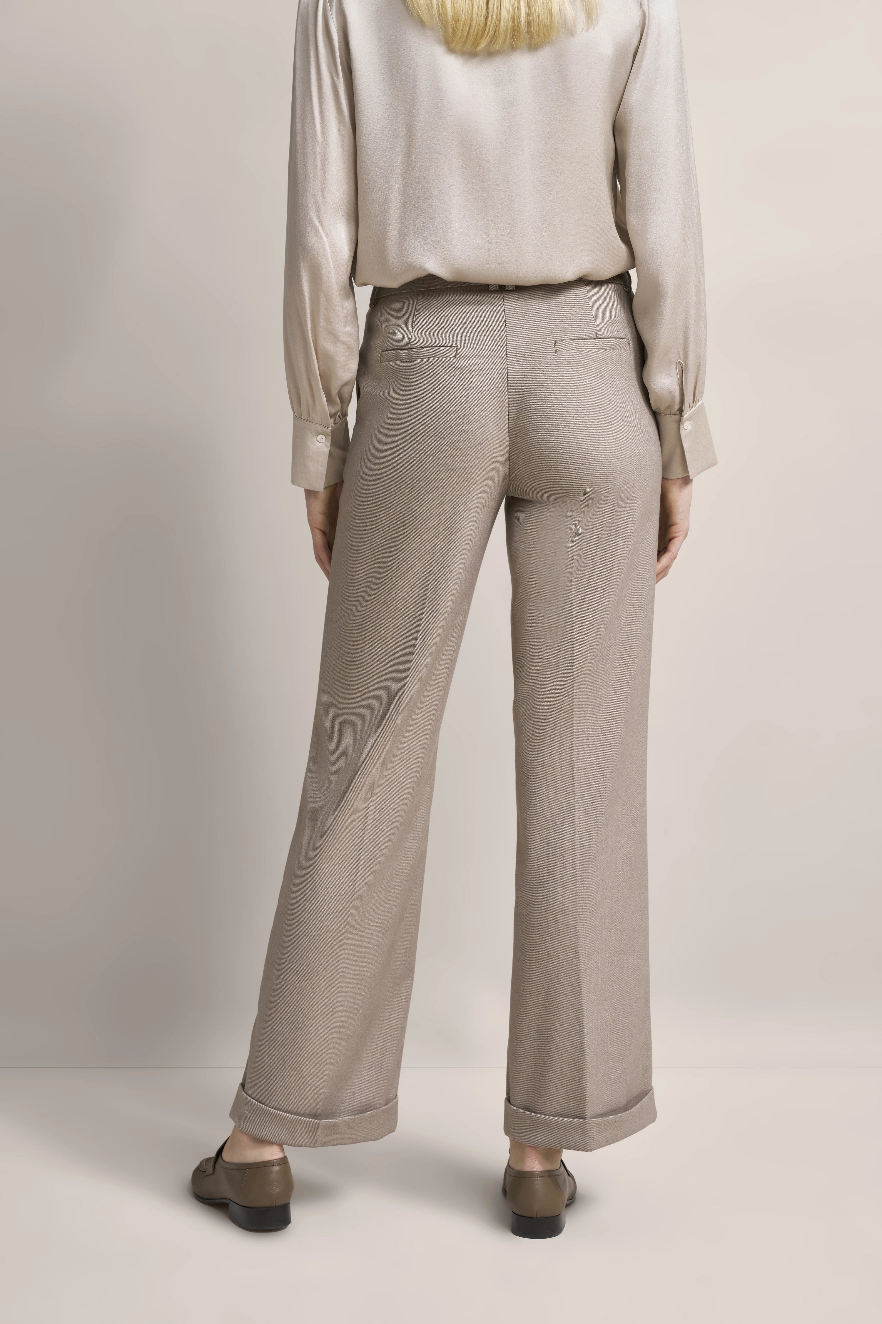 Beige satin blouse and trousers, back view, model posing casually, embodying bugatti's relaxed Italian elegance.