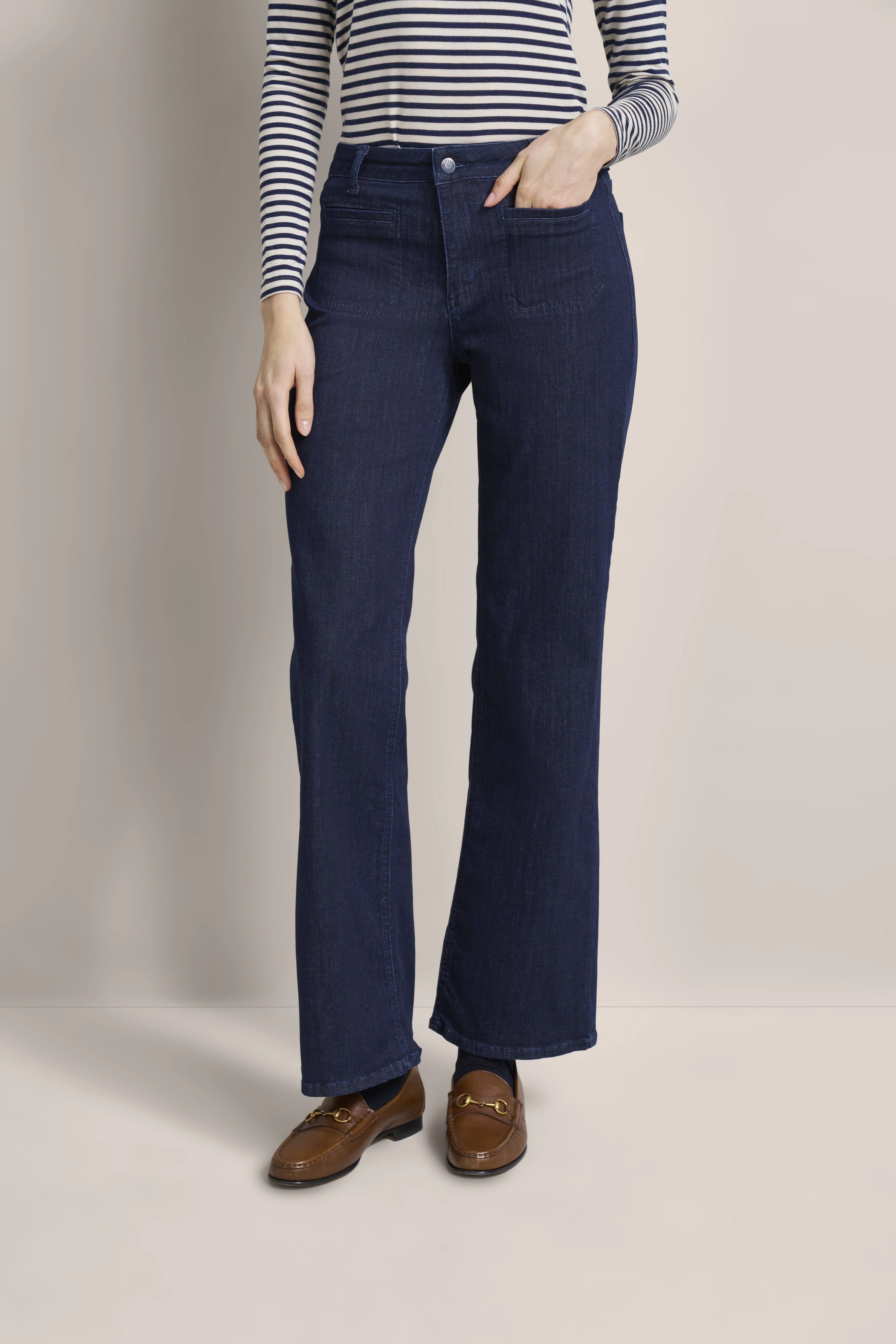 Dunkelblaue Jeans, gestreiftes Oberteil, braune Loafer, legeres Modelbild, entspannte Pose.