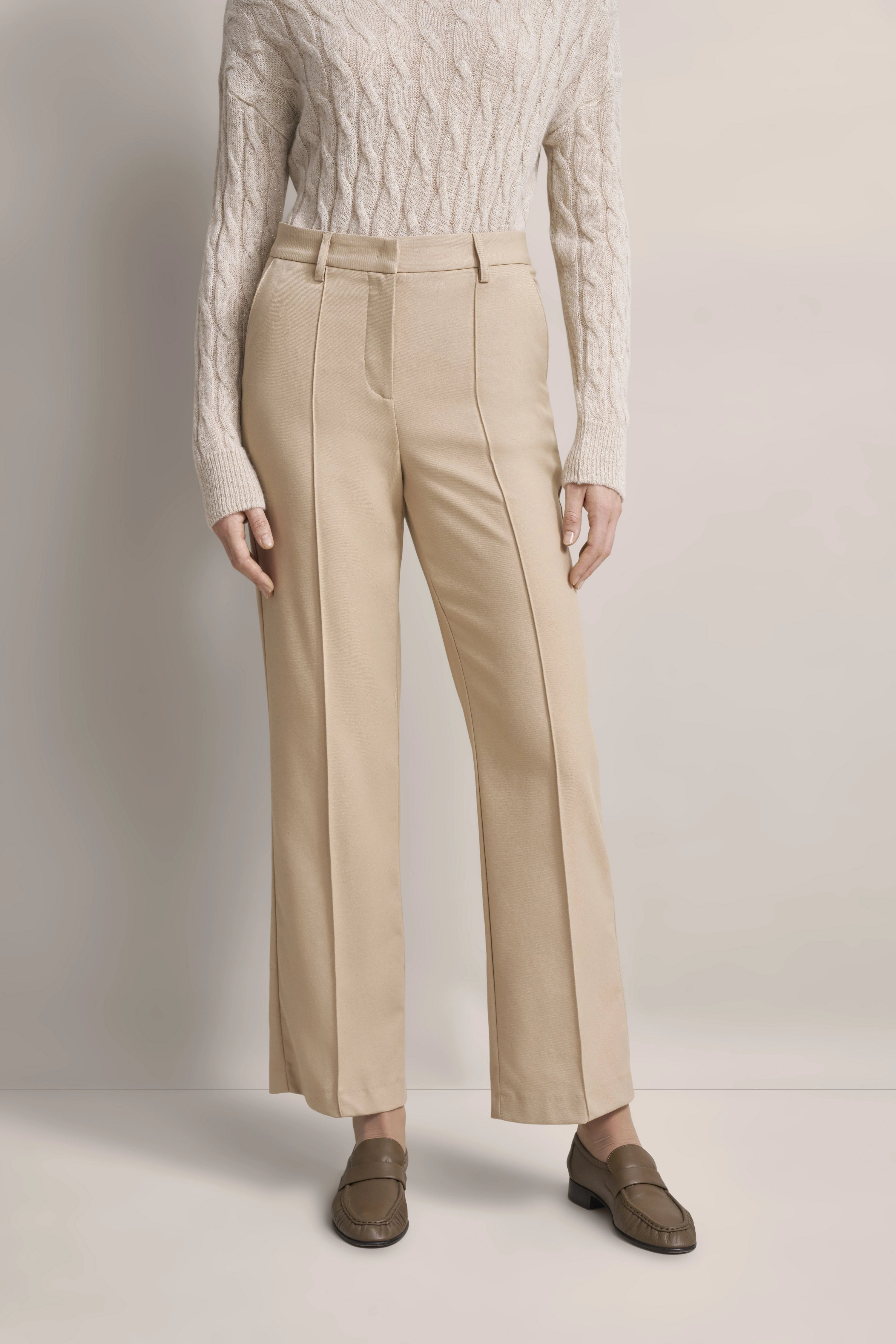 Beige cable-knit sweater and trousers by bugatti. Casual model pose, exuding timeless Italian-inspired elegance.