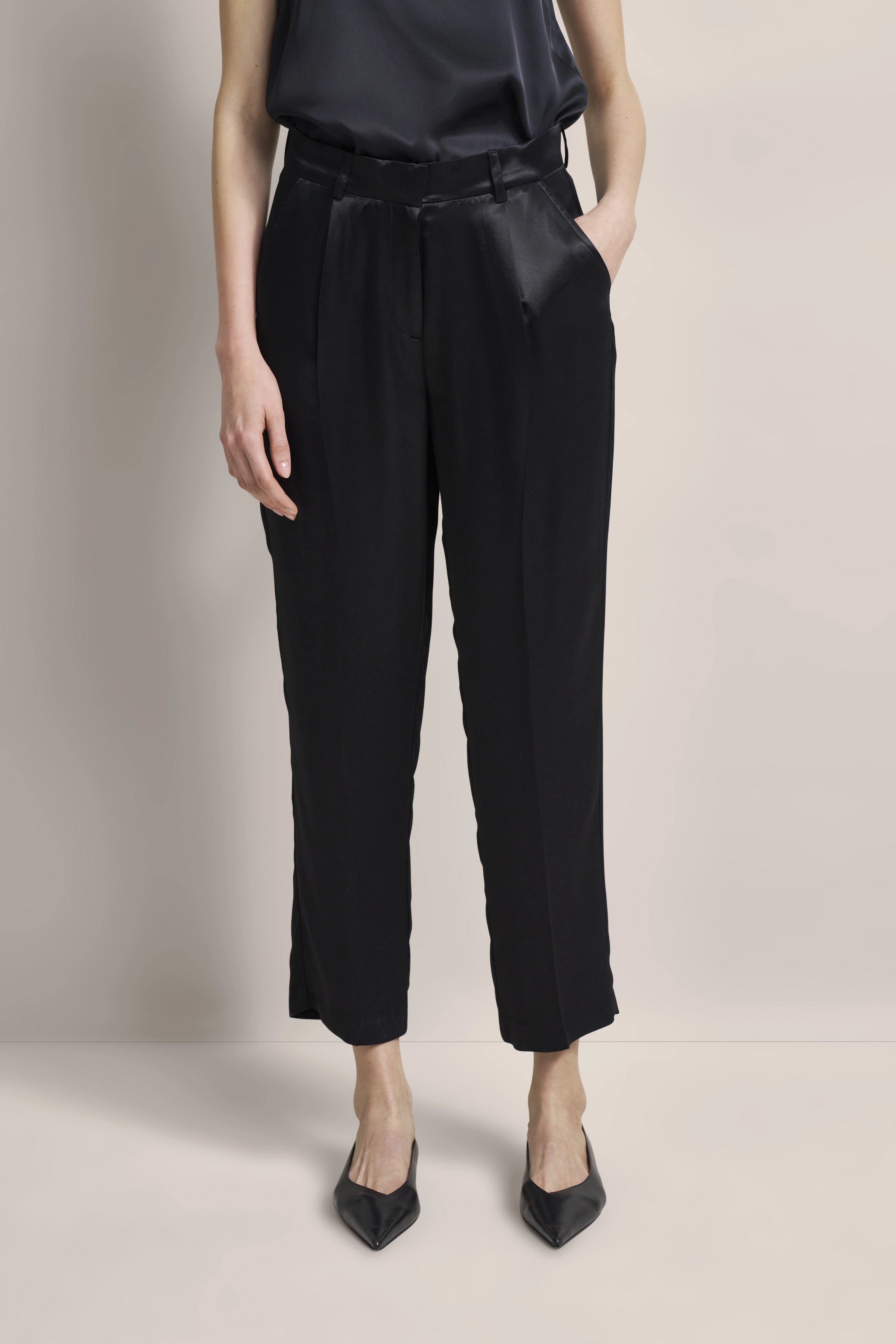 Black bugatti trousers with satin top, model in relaxed pose, elegant and stylish.