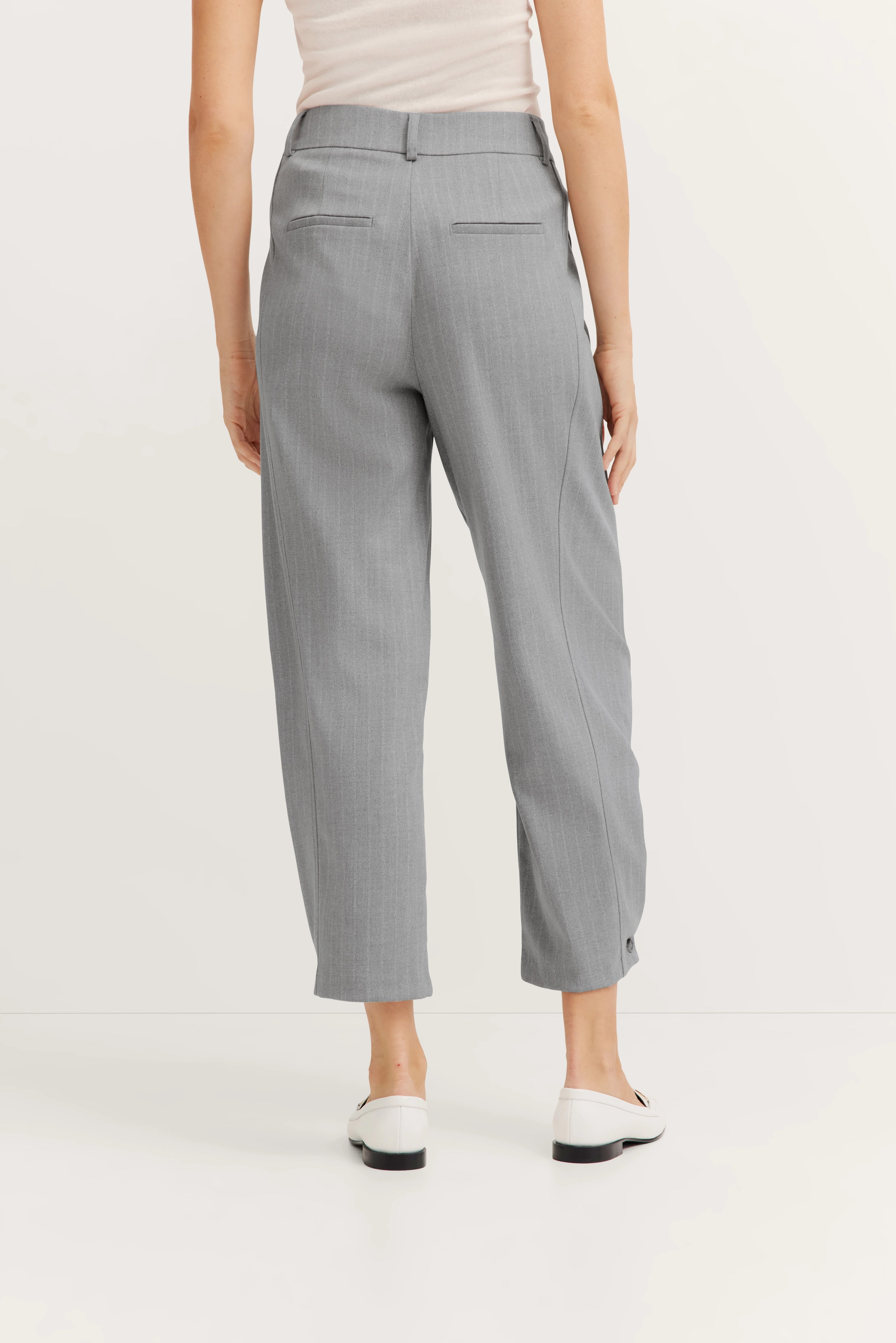 Graue Nadelstreifenhose von hinten, legeres Modelbild, lässige Pose, weißes Oberteil.