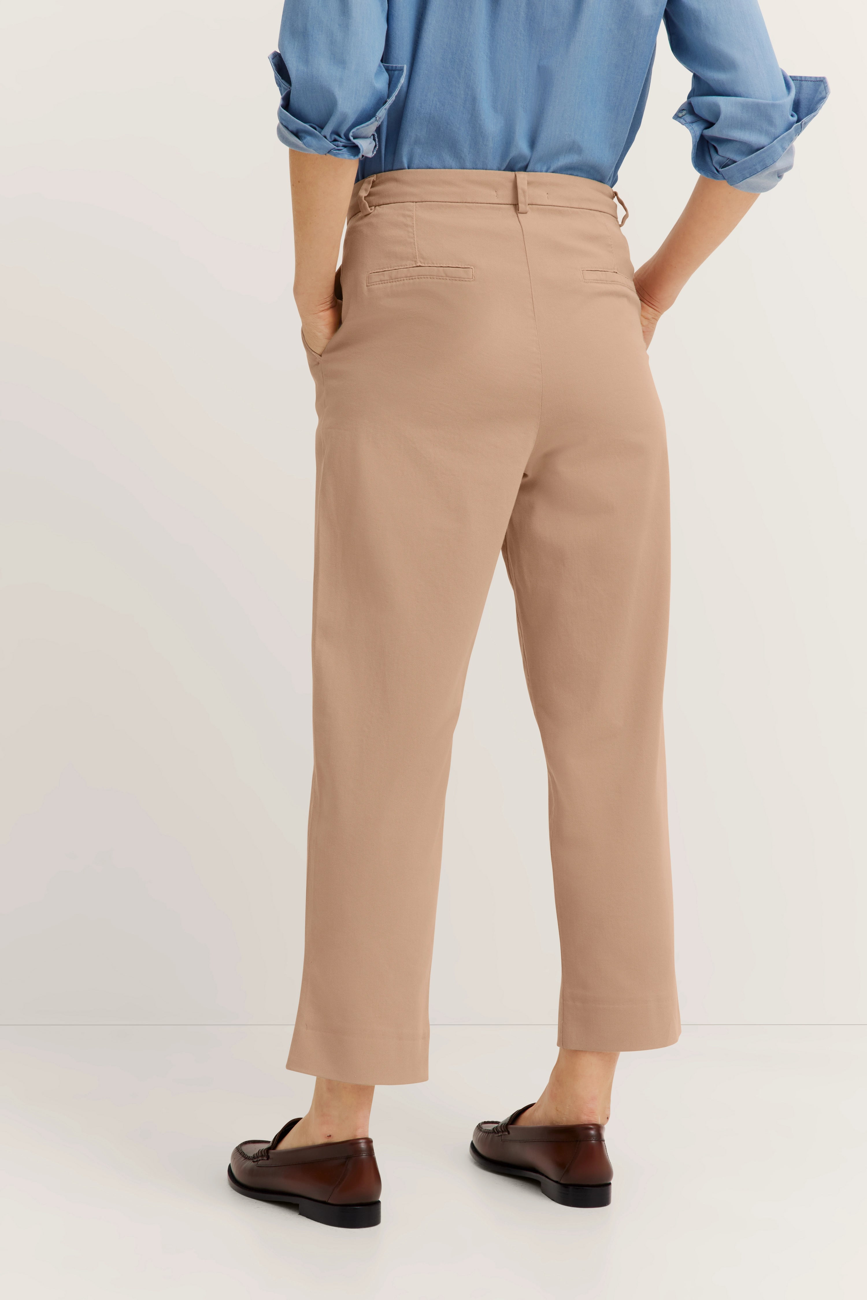 Model in beige bugatti Hose und blauer Bluse, Rückansicht, lässige Pose.