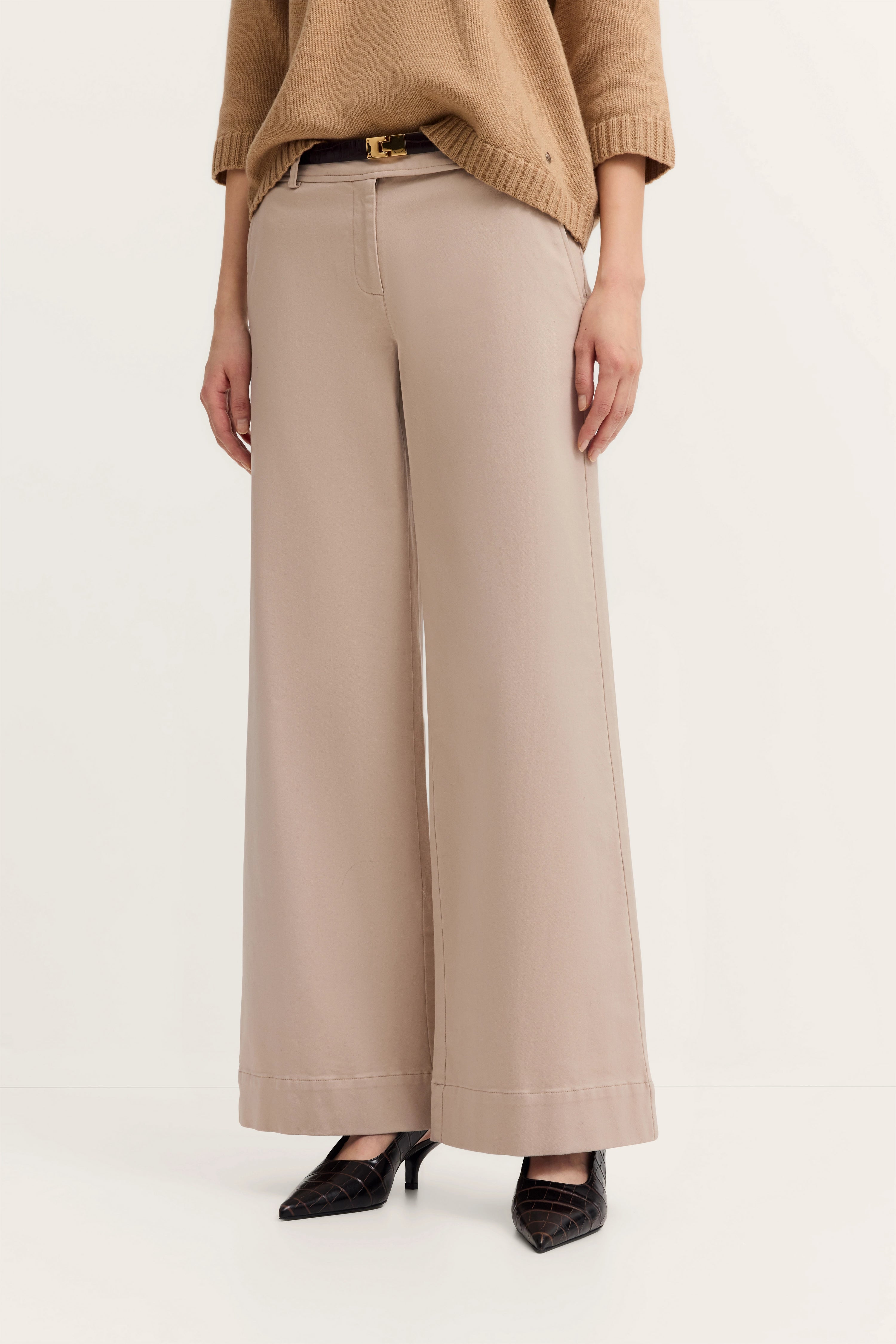 Beige wijde broek en bruine trui, model staat ontspannen, zwarte hakken.