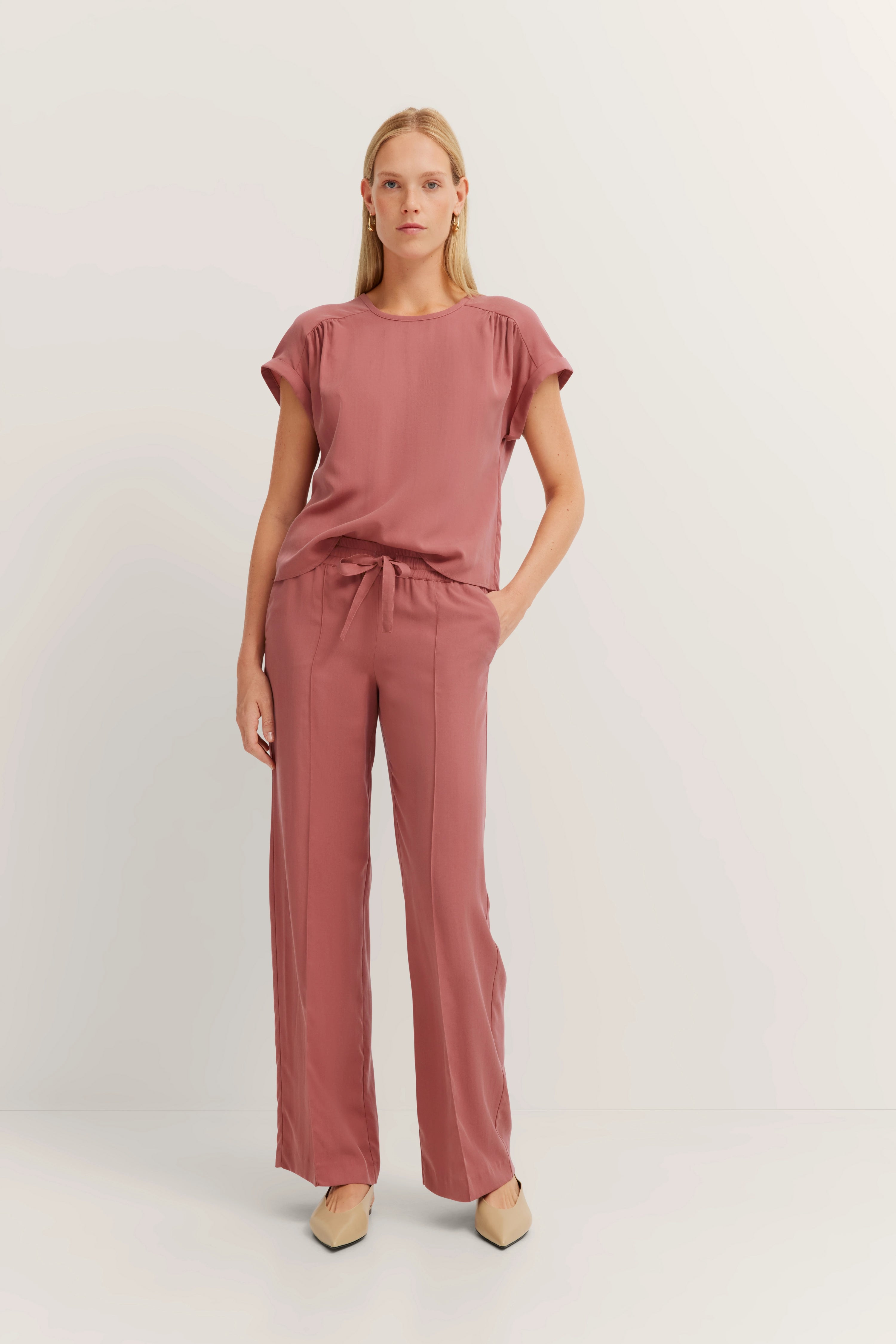 Model in rosa bugatti Set, lässige Pose, entspannter Stil mit kurzen Ärmeln und weitem Bein.