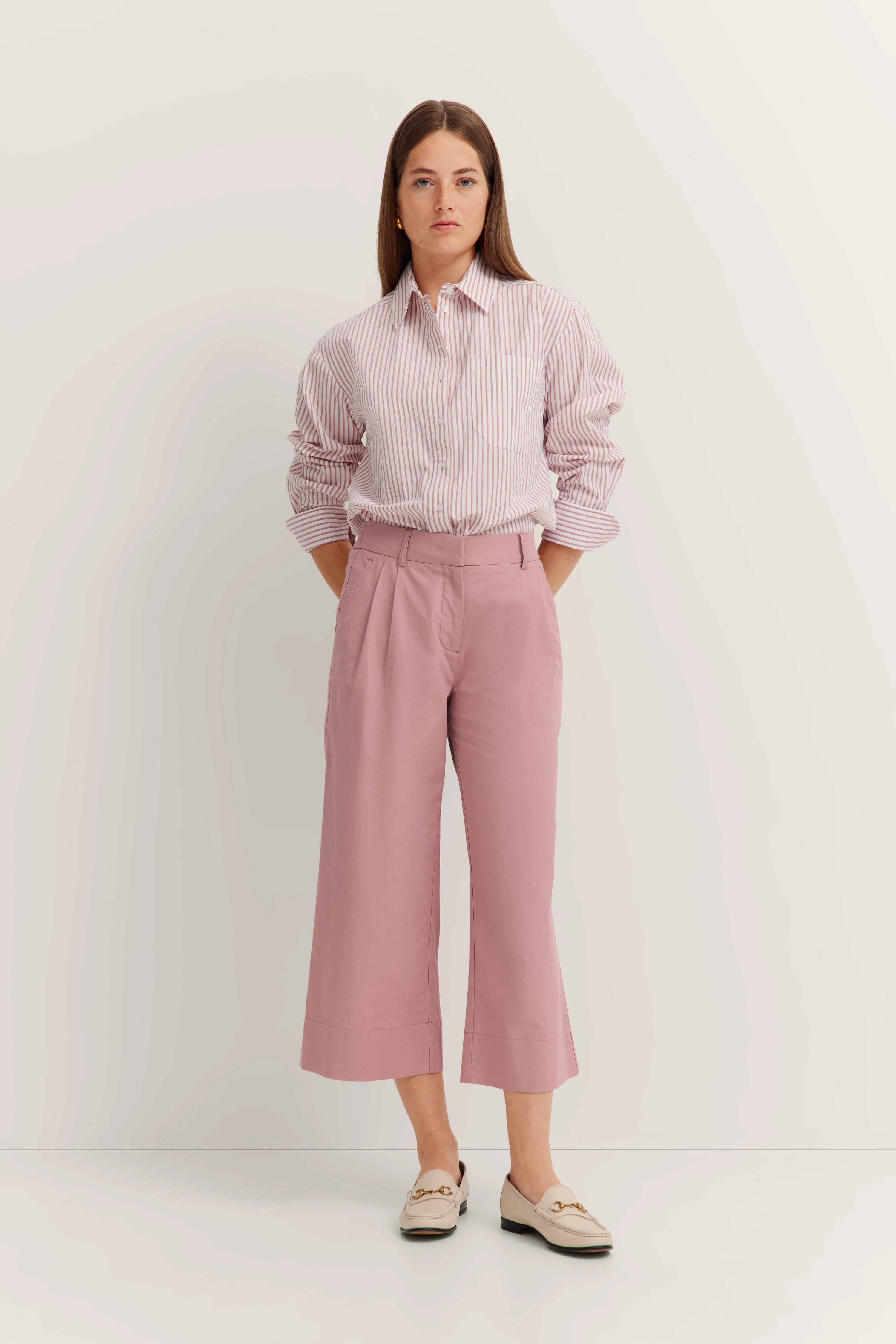 Model in striped bugatti shirt and pink pants, hands in pockets, relaxed pose.
