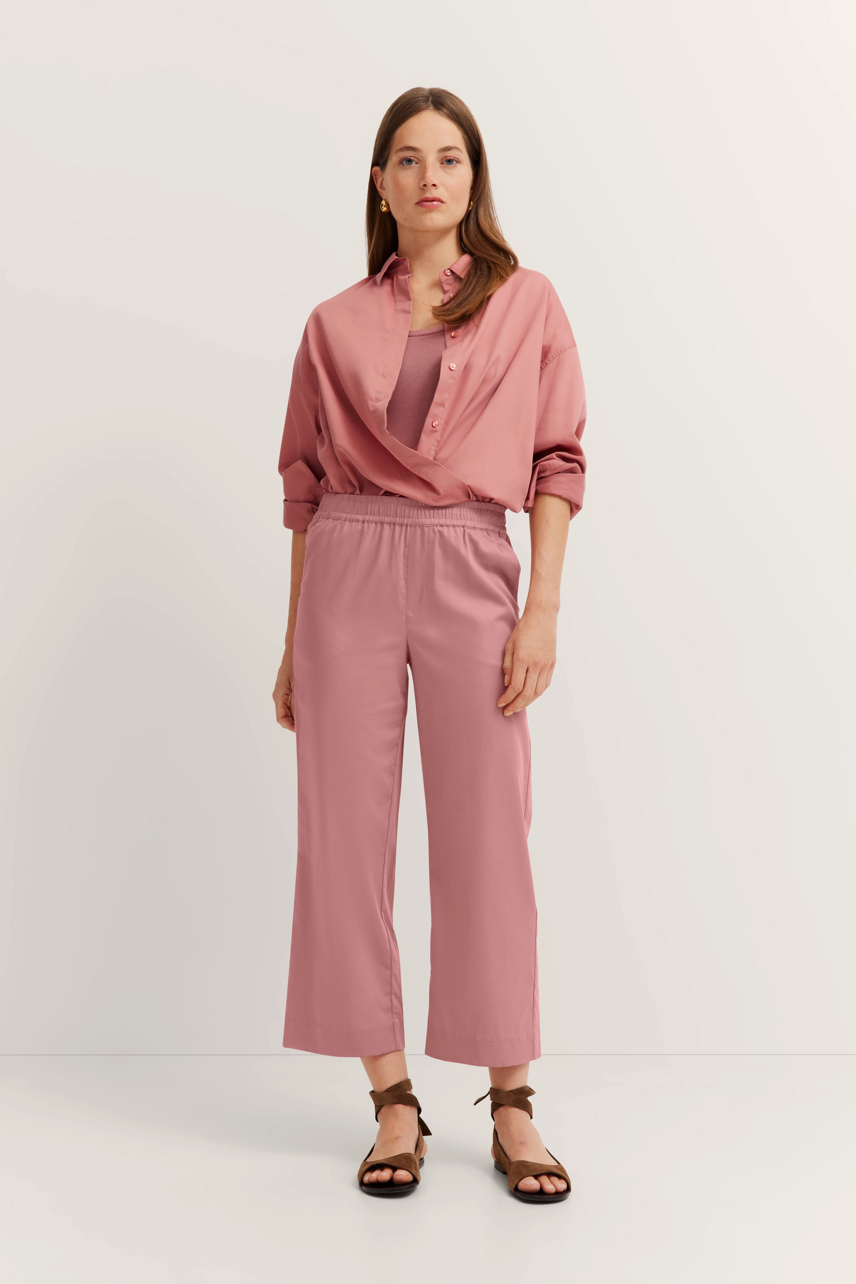 Model in pink bugatti outfit, blouse loose over top, wide pants, relaxed pose.
